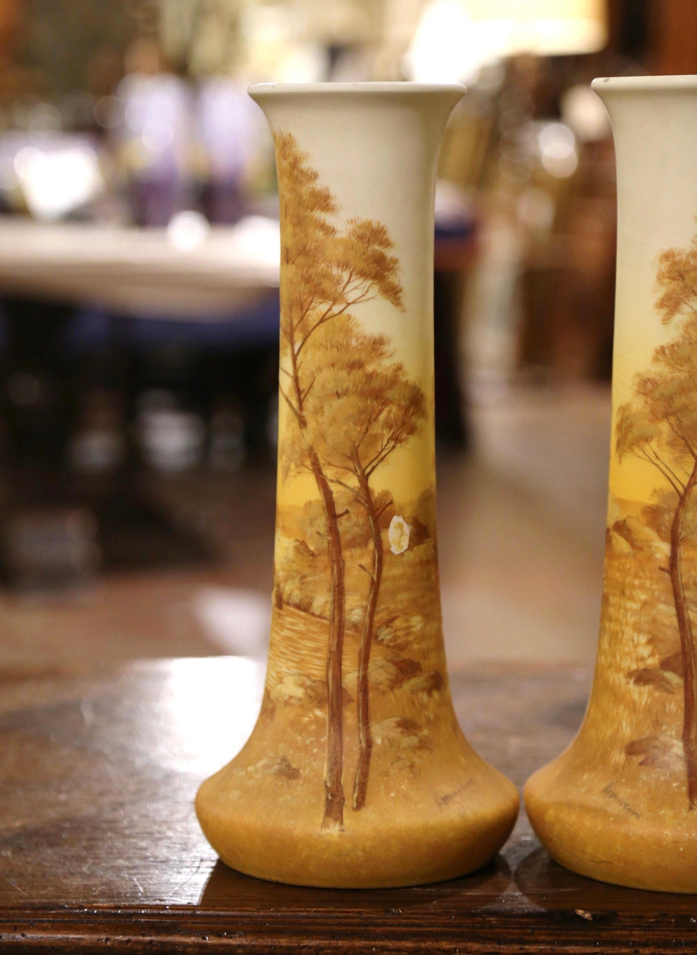 Décorez une cheminée ou une console avec cette élégante paire de vases en émail ancien. Créés dans le sud de la France, ces vases colorés ont un long col sur une base circulaire ; chaque vase présente une scène côtière typique de la Côte d'Azur avec