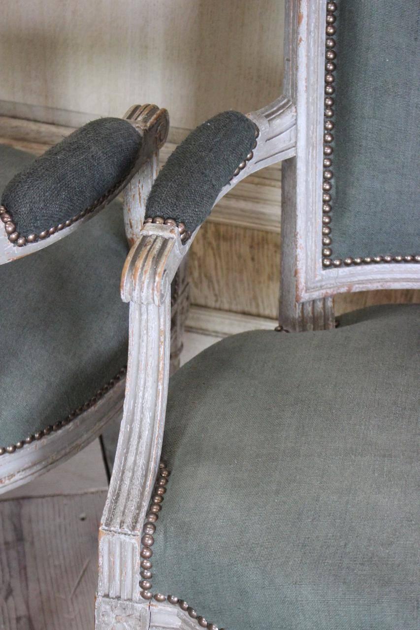 A very elegant pair of 19th century French painted fauteuils, in the Louis XVI taste, retaining their original paint and having been reupholstered by us in an antique hand dyed linen.