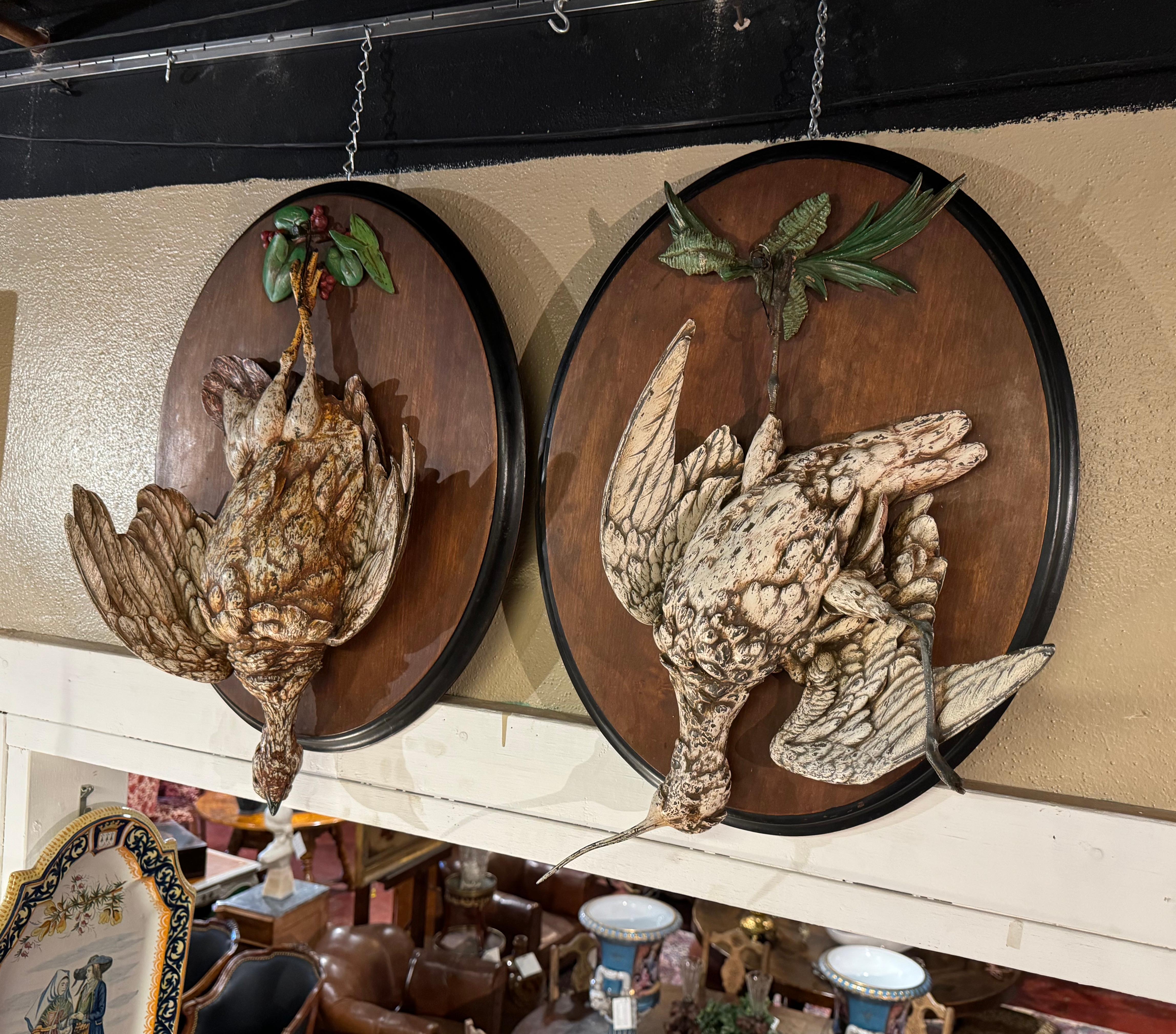 These large heavy antique trophy plaques were created in France, circa 1880. Set on oval walnut board, each wall hanging decor feature a detailed spelter carved bird in high relief, tied upside down to foliage embellishments with a rope at the base.