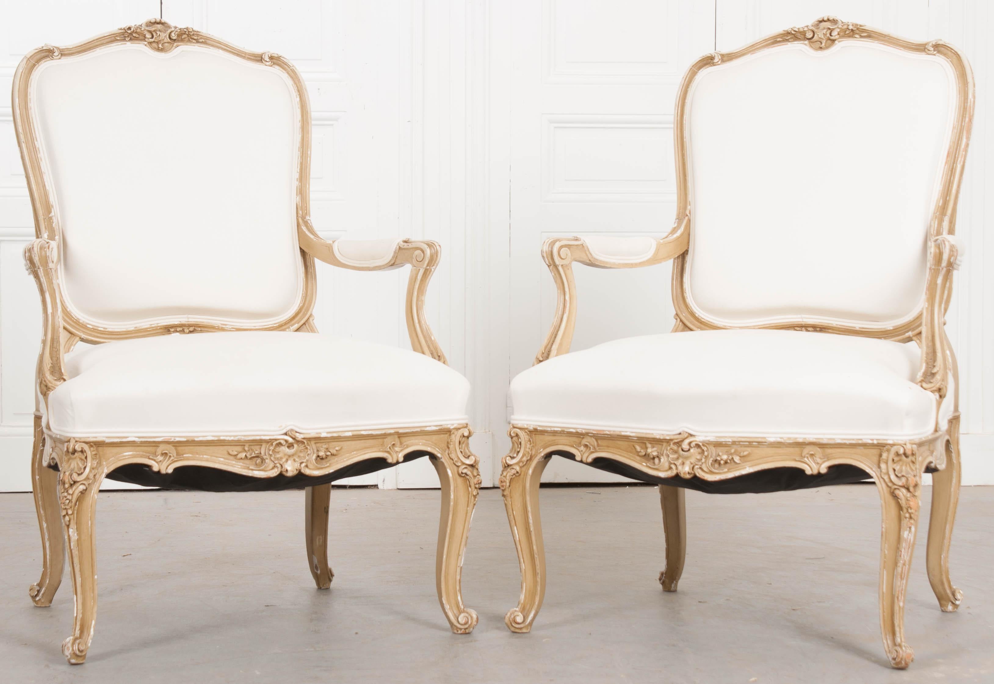 A gorgeous pair of upholstered French 19th century Louis XV style fauteuils, painted in an antique cream/taupe color. The frames are ornately decorated, with Louis XV motif carvings found all over. The pair have been more recently upholstered in an