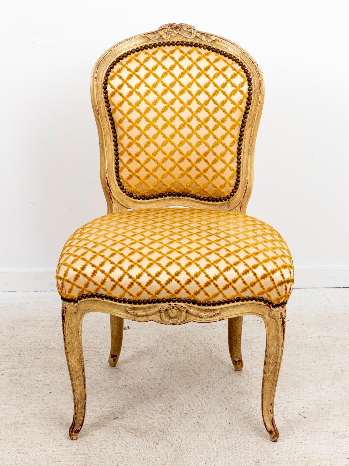 Circa 19th century pair of French painted side chairs in the Rococo revival style with cabriole legs and carved floral motifs on the seat back. Please note of wear consistent with age including finish loss and paint loss.