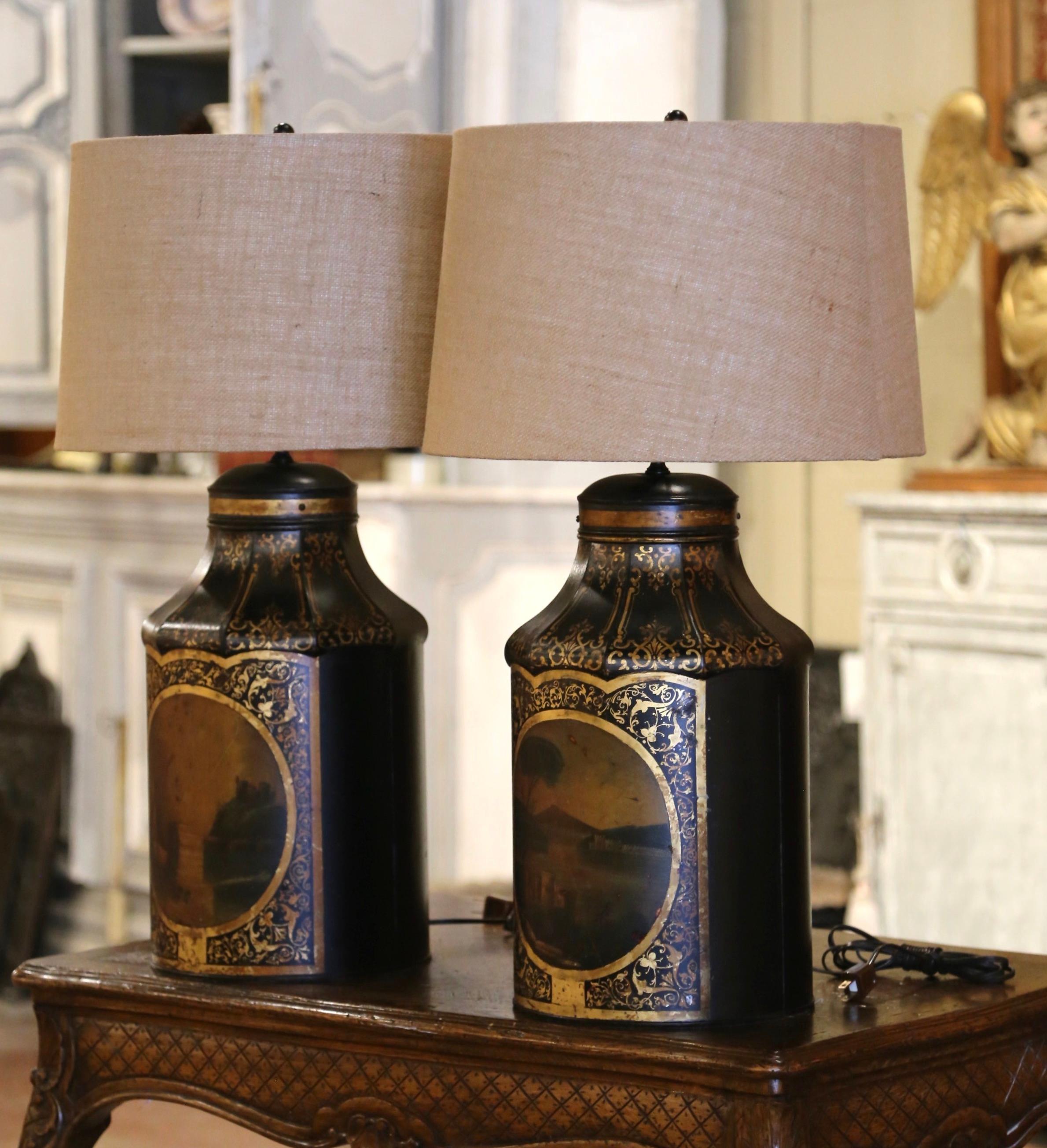 Decorate bedside tables in a master bedroom, or side tables in a living room with this elegant pair of antique lamps. Created in France, circa 1890 and made of tole, each large tea box features two hand painted medallions with harbor and coastal
