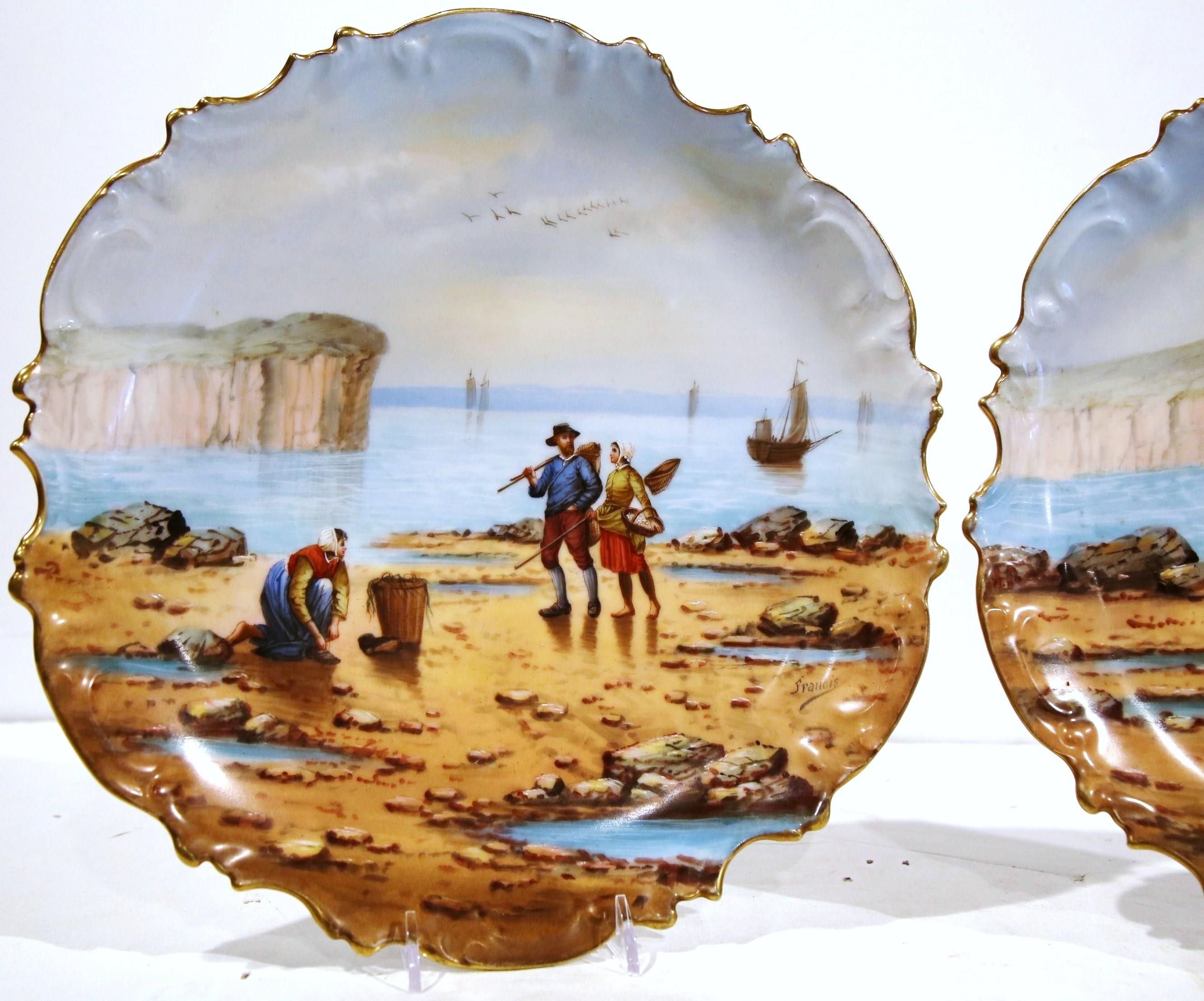 These elegant decorative plates were crafted in Paris, France, circa 1870. The hand painted platters with scalloped edges, depict two beach scenes on the coast of Brittany; each wall decor features people fishing shrimp and mussels. The antique