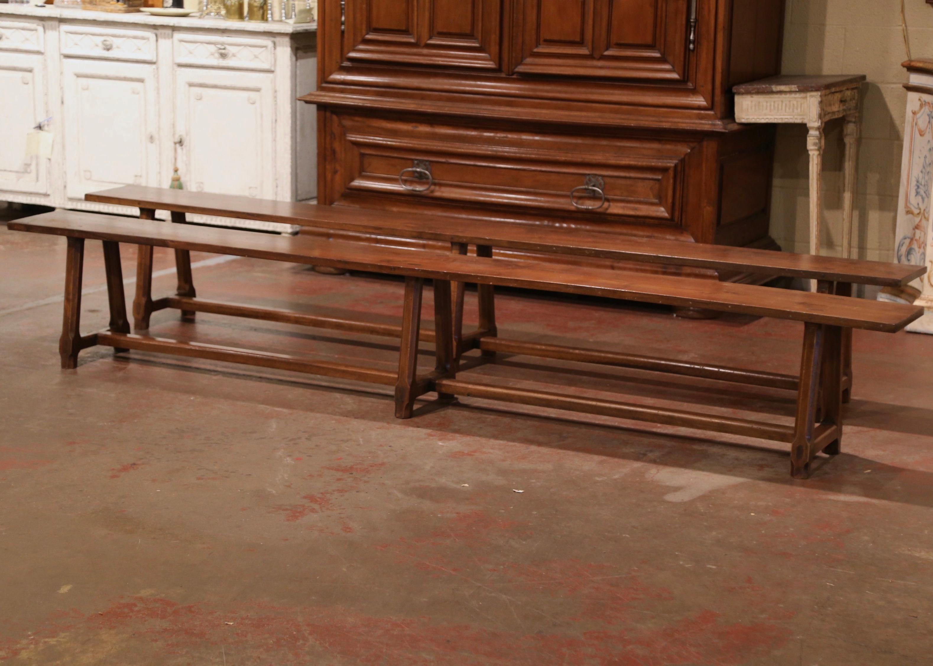 Dressed a farm table with this elegant pair of antique provincial benches. Crafted in the Poitou region of France, circa 1890, and carved of cherry wood, each farmhouse bench stands on three angled octagonal legs with visible mortise and through