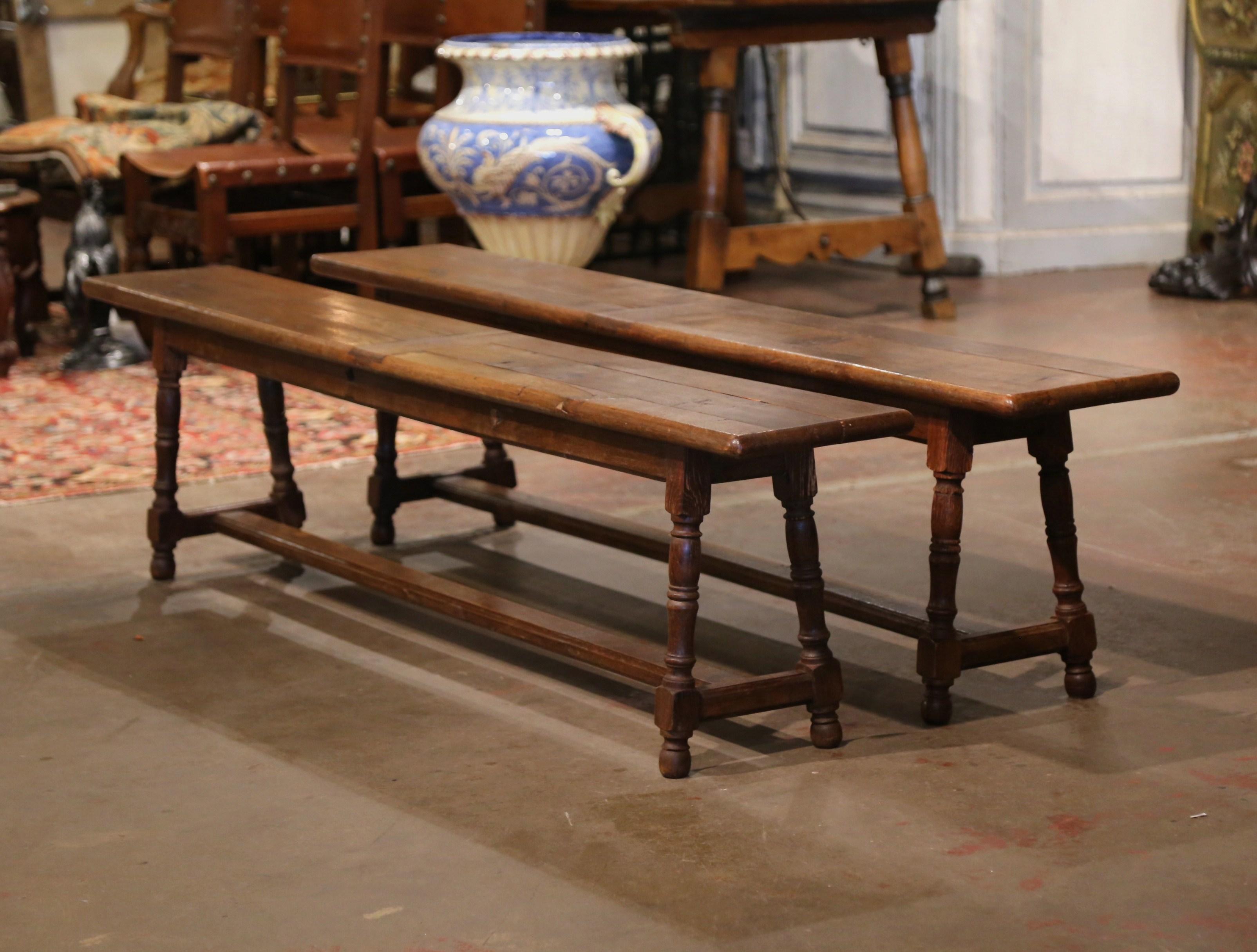 Dressed a farm table with this elegant pair of antique provincial benches. Crafted in the Normandy region of France, circa 1880, and carved of oak wood, each farmhouse bench stands on a pair of angled turned legs connected with a bottom stretcher.