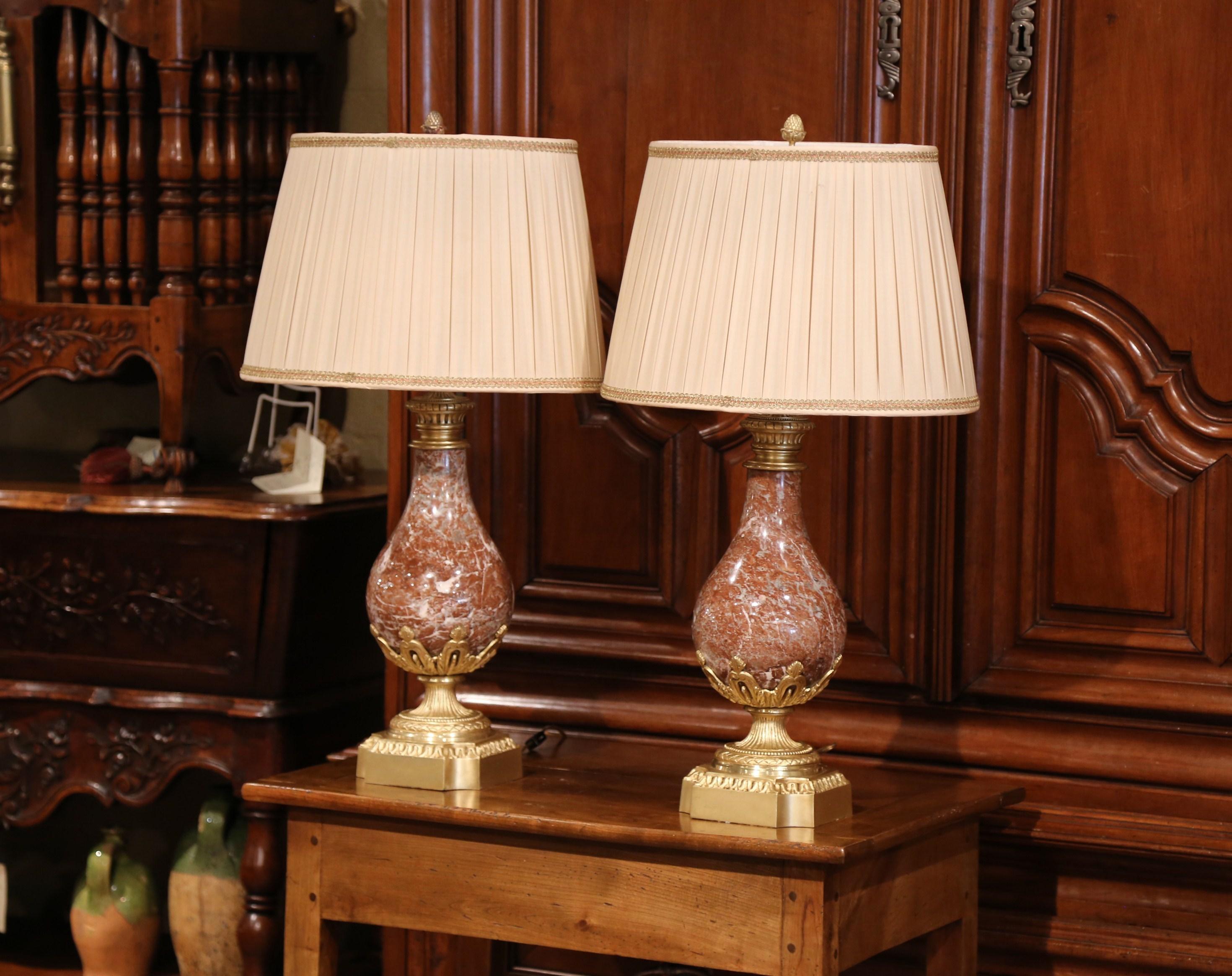 Crafted in France circa 1860, each cassolette is made of carved red marble and is embellished with a bronze base and decorative mounts. The large vessels have been converted into a table lamps decorated with custom, pleated white shades. The urns