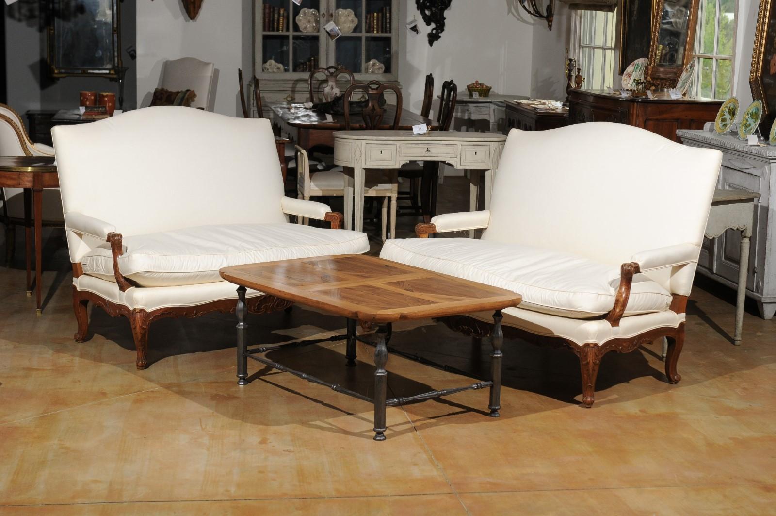A pair of French Régence style wooden canapés from the 19th century, with cabriole legs, acanthus leaves and new upholstery. Born in France during the politically dynamic 19th century, each of this pair of sofas features a slanted camelback,