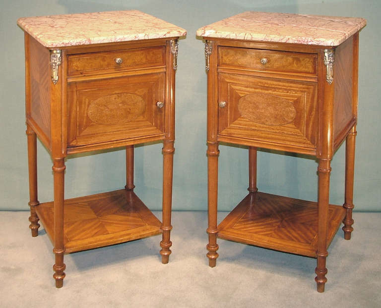 A pair of late 19th century French satinwood freestanding bedside cabinets having cottanello antico marble tops with frieze drawers above amboyna panelled doors and cupboards retaining original porcelain interiors. The cabinets, with gilt metal