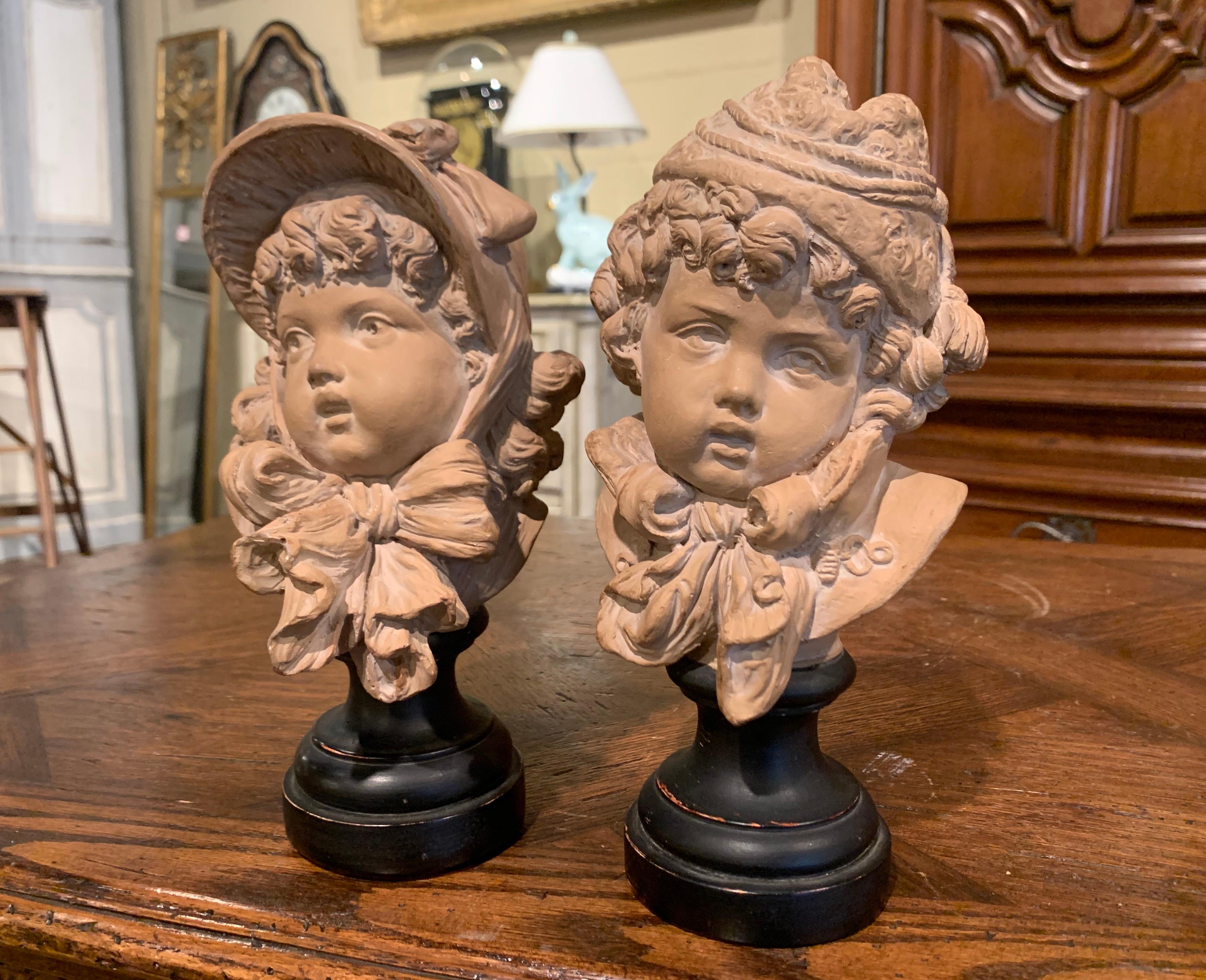 Decorate an office shelf with this cheerful pair of antique terracotta children busts. Crafted in Paris, France circa 1880, each subject features a child face sculpture standing on a black painted socle base. Each figure has wonderful facial