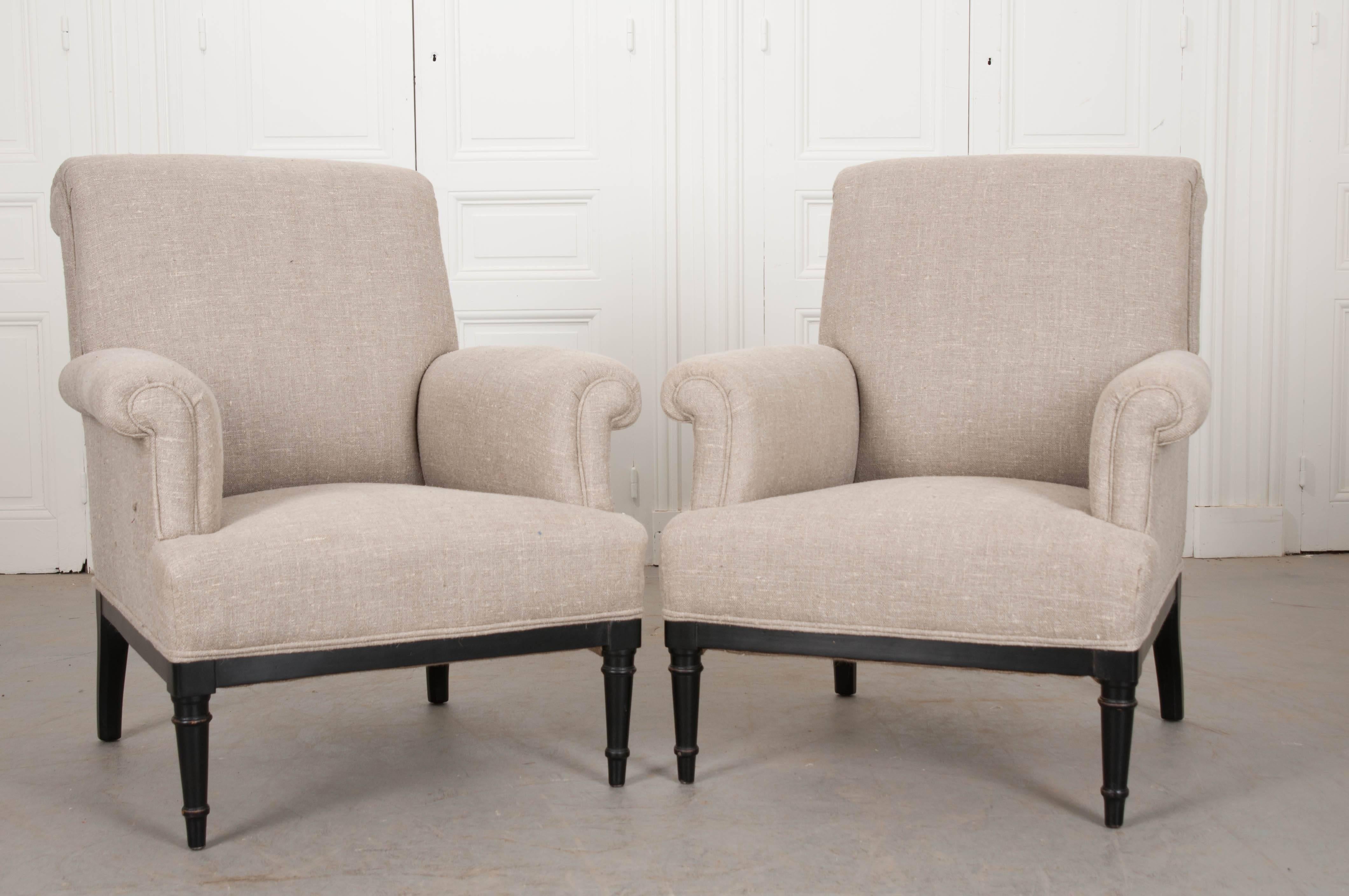 This fabulous pair of 19th century French bergères has been recently reupholstered in a neutral slubby linen. The pair have a classic design with rolled backs and arms and double welt cording where the upholstery meets the ebony base. The base has