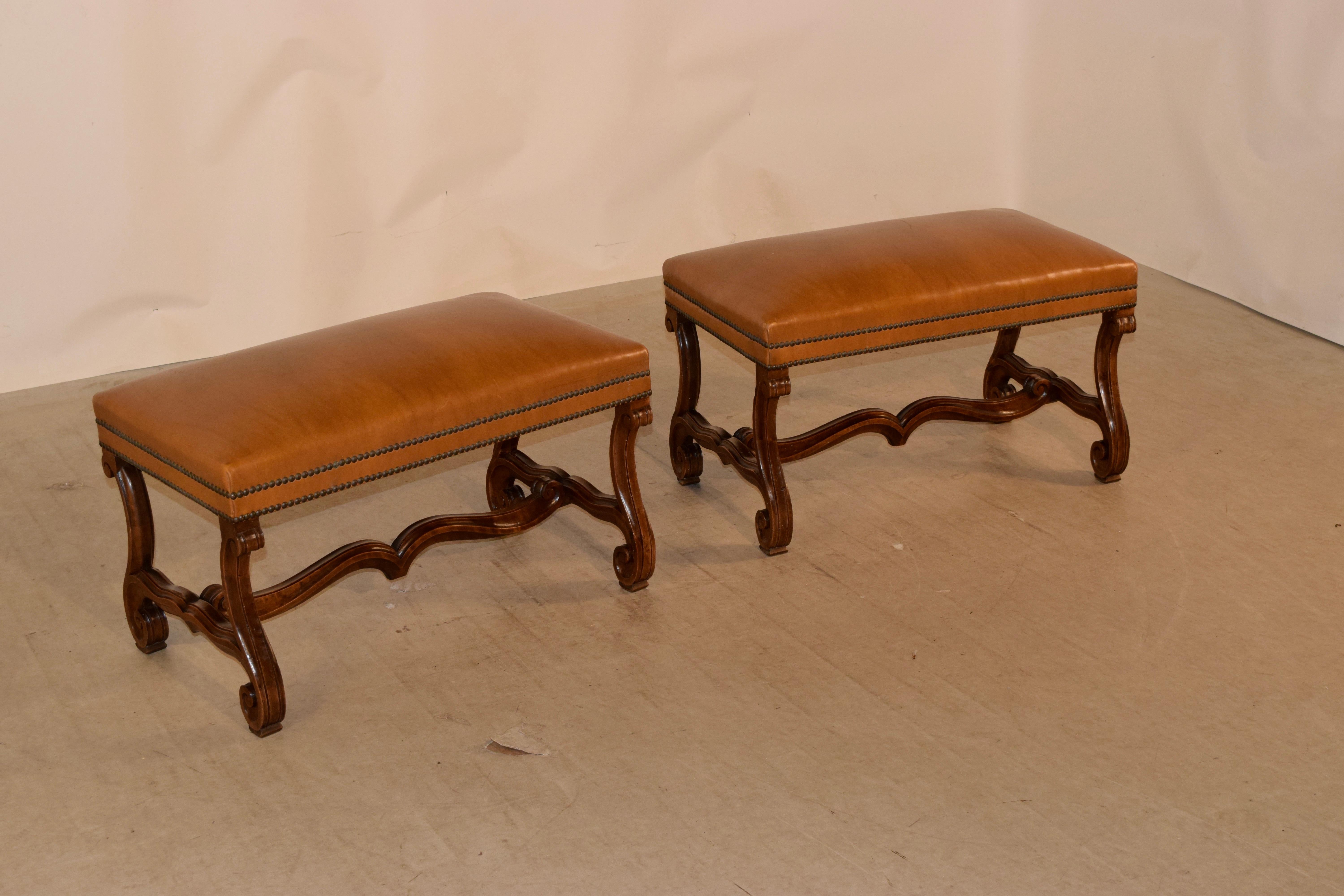 Pair of 19th century French walnut benches with mutton leg bases and leather upholstery. These French benches feature rectangular seats upholstered with leather and finished with brass nailhead trim, supported on mutton legs these legs are connected