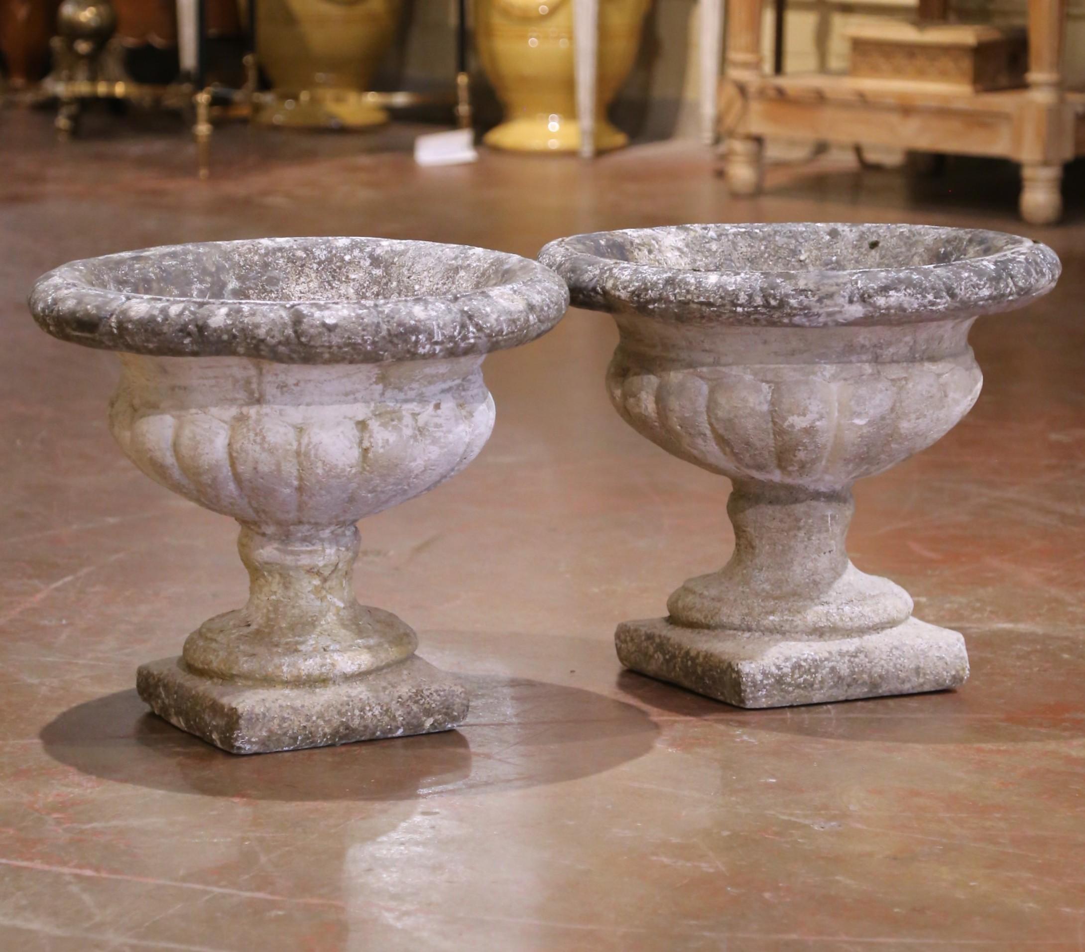 This pair of antique garden urns was crafted in Normandy, France, circa 1880. Made of hand-carved stone, each urn features a classic Campana form with a lobed body and wide, rounded rim. Resting on a square plinth base, the shapely silhouette is