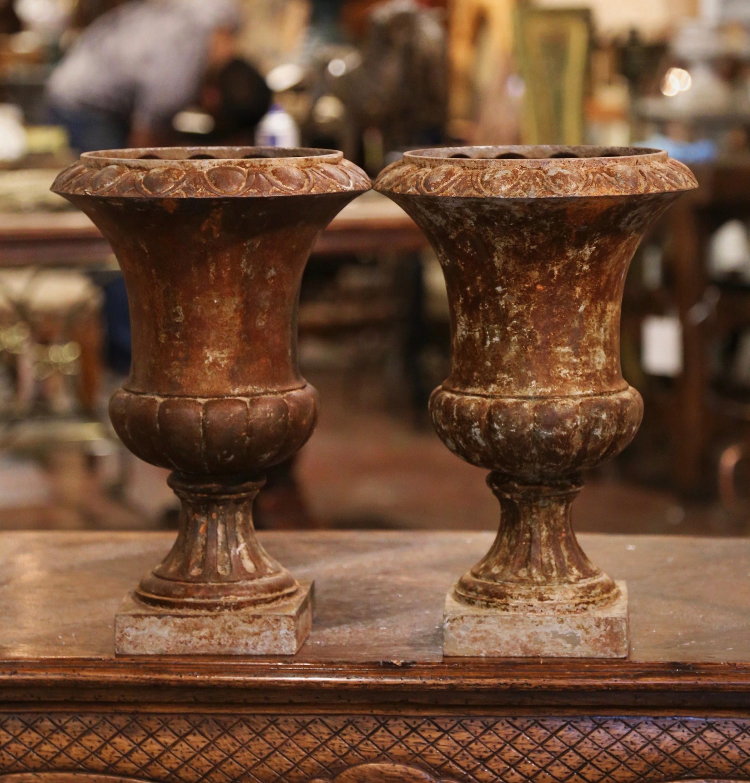 Decorate a backyard or a patio with this elegant pair of classical Roman antique urns. Crafted in France circa 1850, each vase stands on a square base with pedestal over a gadrooned body and ending with a wide mouth with flared rim at the top. The