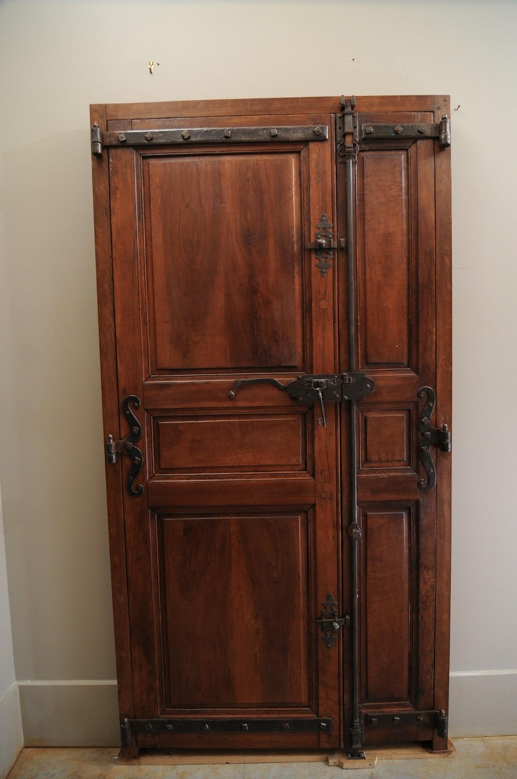 A pair of French wooden communication doors from the 19th century, with raised panels and iron hardware. Created in France during the 19th century, this pair of communication doors features a perfectly organized arrangement of panels adorned with