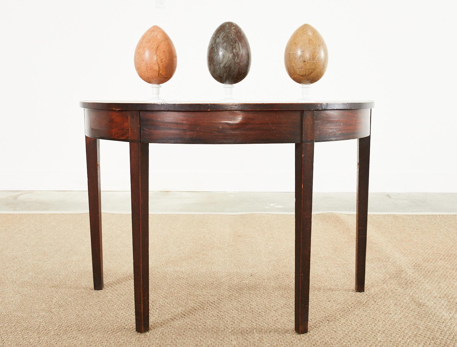 Handsome pair of 19th century Georgian demi-lune console tables crafted from mahogany. Prior ends of a large Georgian banquet table that fit together to form a 42 inch round circle. The tables feature radiant mahogany veneered friezes supported by
