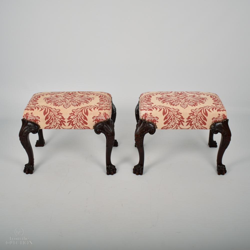 A pair of 19th century Georgian mahogany footstools in the George II style. A beautiful pair of stools in excellent condition currently upholstered in a contemporary fabric. On four finely carved mahogany legs onto clawed feet.