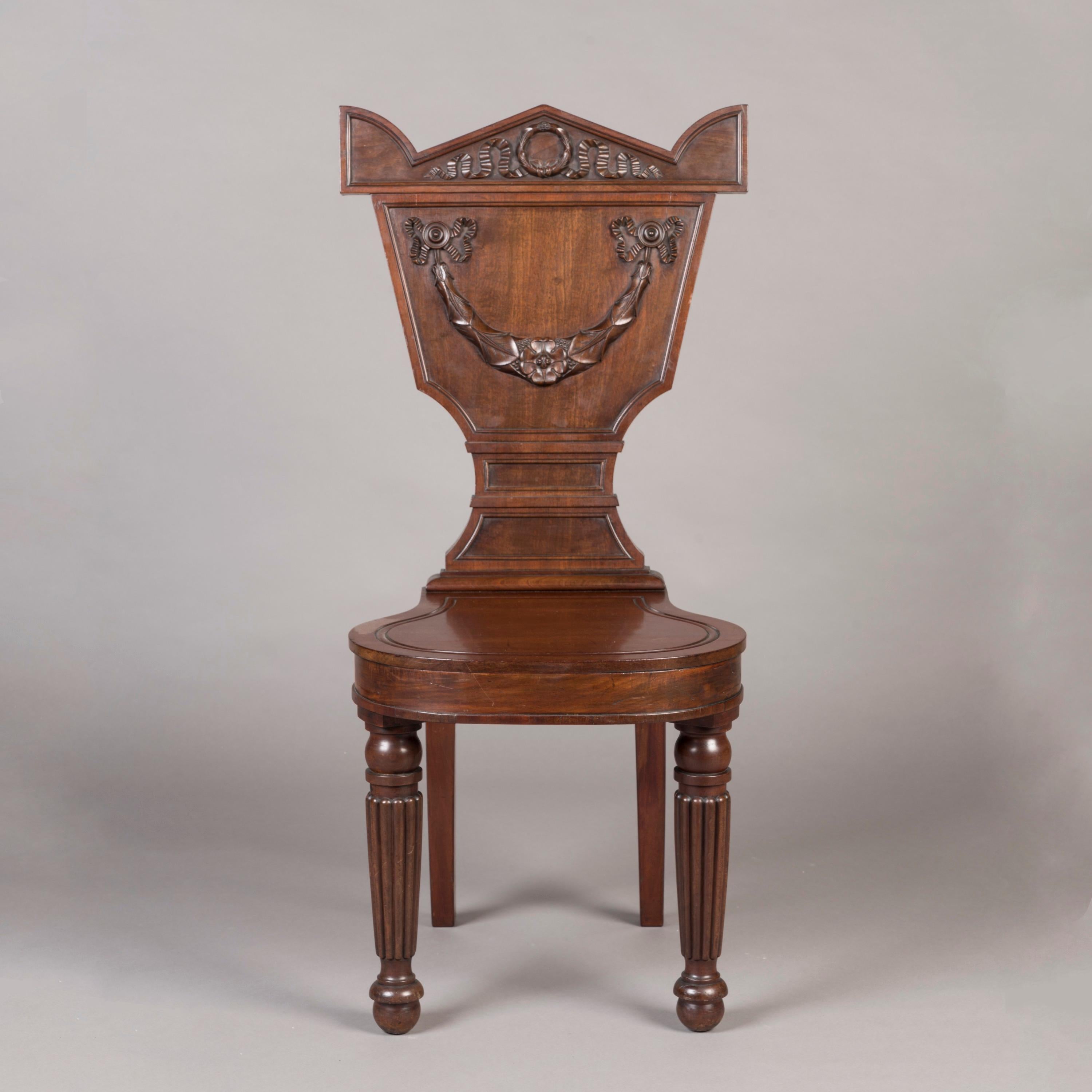 A Pair of George IV Hall Chairs
By William Latham Huxley

Constructed in mahogany, having beautifully turned and reeded front legs and elegant sabre legs to the rear, the back rest of a most unusual waisted shape and adorned with carved garlands,