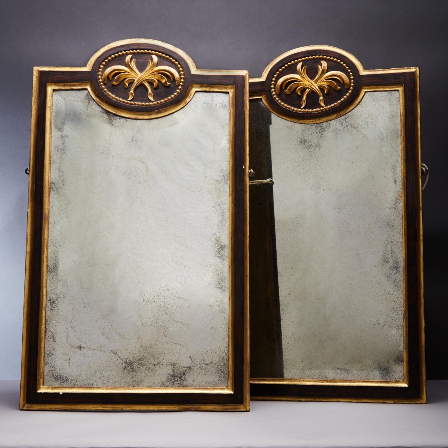 The pair antique gilt and ebonized mirrors with a central cartouche above of a leaf motif. The frames are made of carved wood and gesso a thin layer of gold leaf is then applied over the surface. Set into the frame the aged oxidized mirror gives a