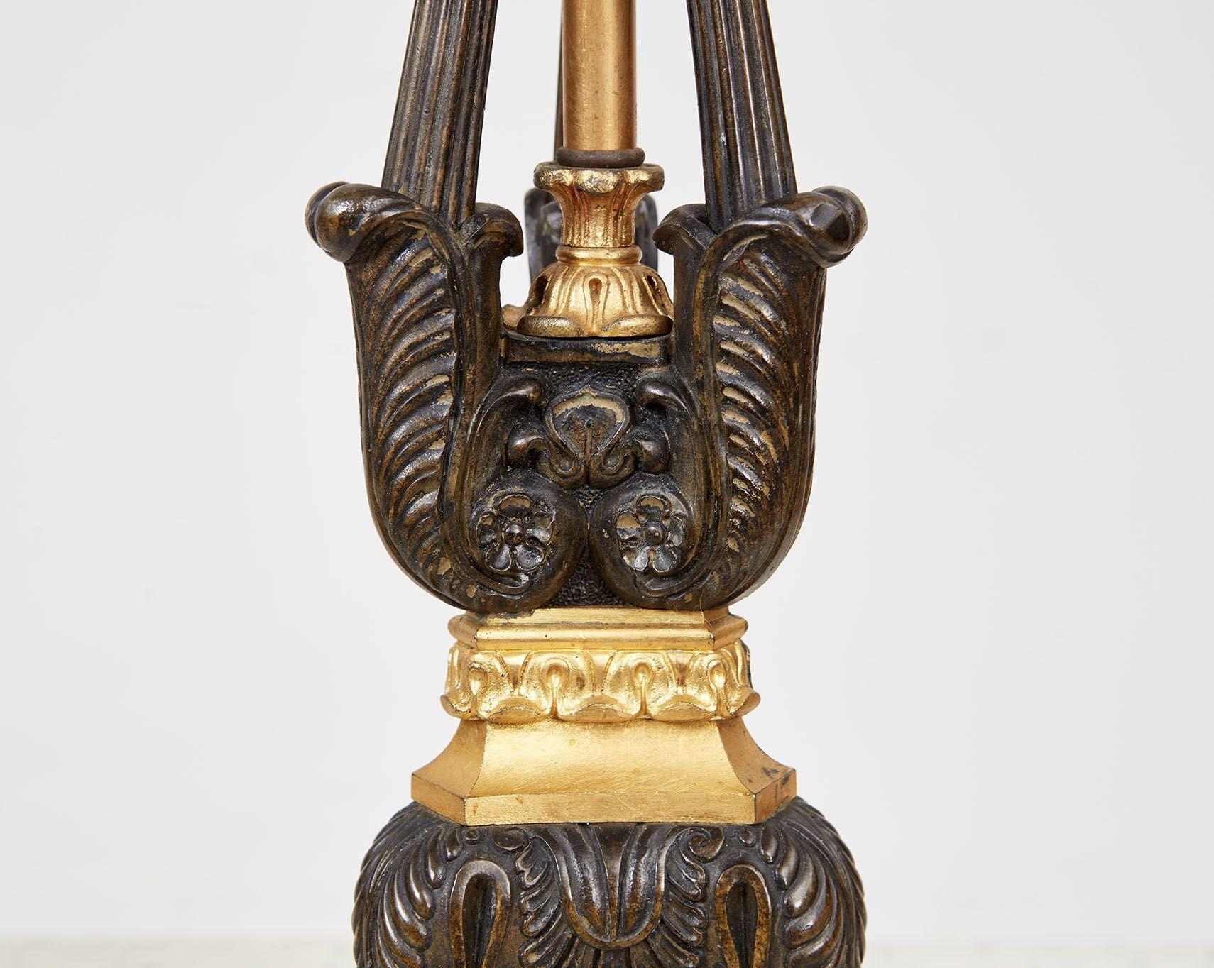 Paire de chandeliers en bronze patiné et doré du 19ème siècle, maintenant utilisés comme lampes, avec des détails d'acanthes et de feuilles de lotus, trois supports à volutes et une base tripartite.