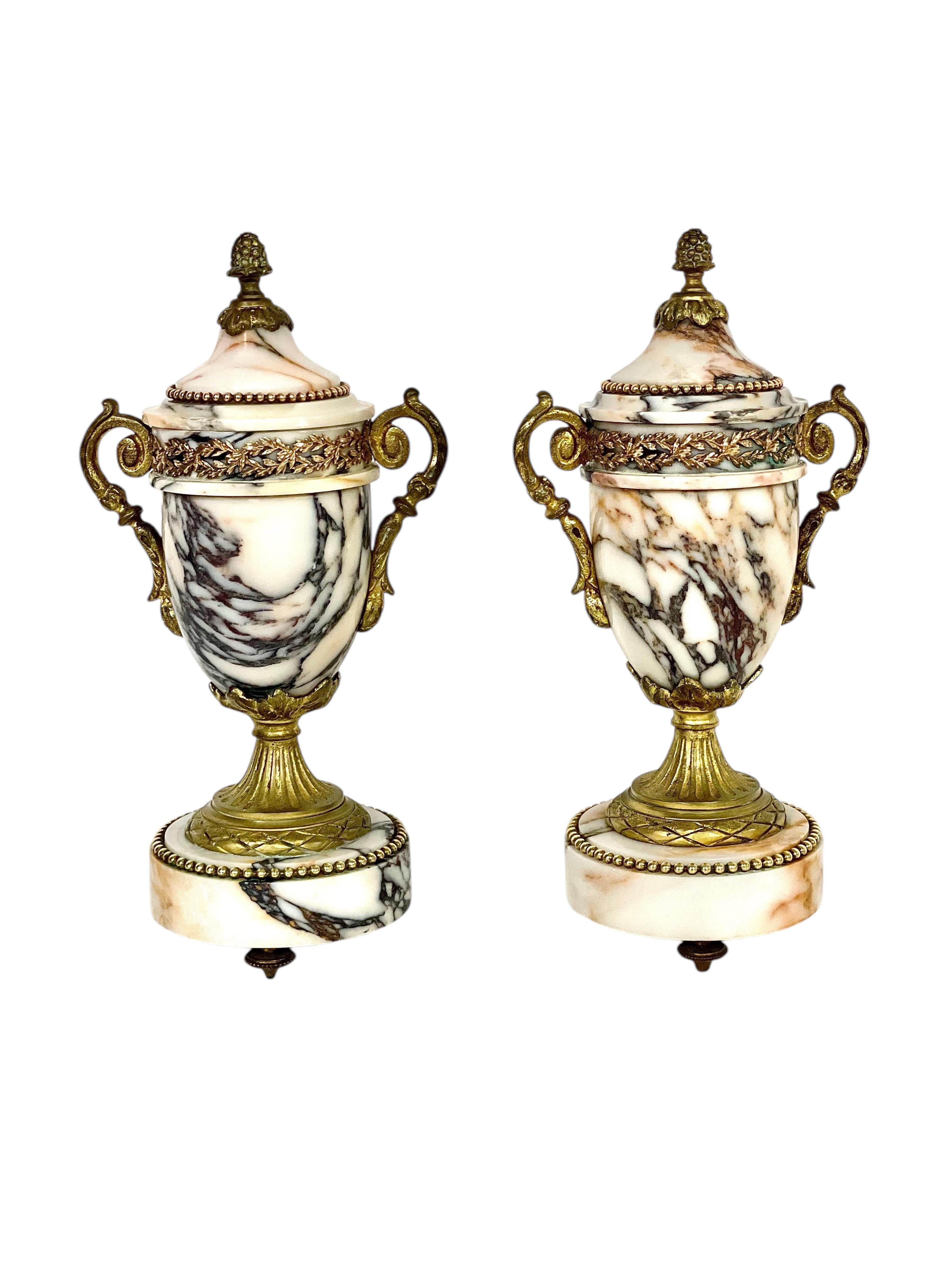 Questa squisita coppia di antiche cassolette francesi è una vera e propria testimonianza dell'arte della fine del XIX secolo. Realizzate meticolosamente, queste urne decorative sono composte da uno splendido marmo venato dai toni caldi del bianco,