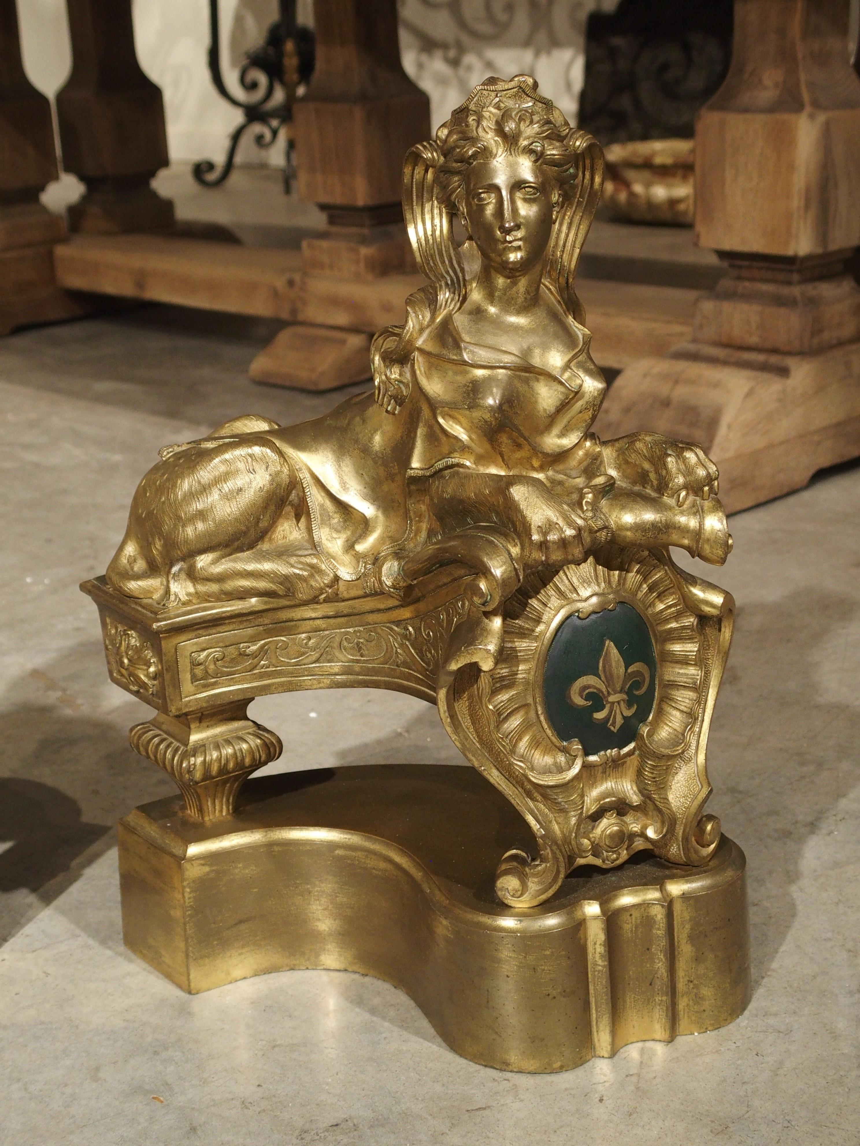This impressive pair of chenets are made of gilt bronze and feature a rich blue rocaille cartouche with Fleur de Lys. They are based on the original sphinx chenets by Guillaume de Grof (1680-1742), a Parisian trained Flemish sculptor who would go on