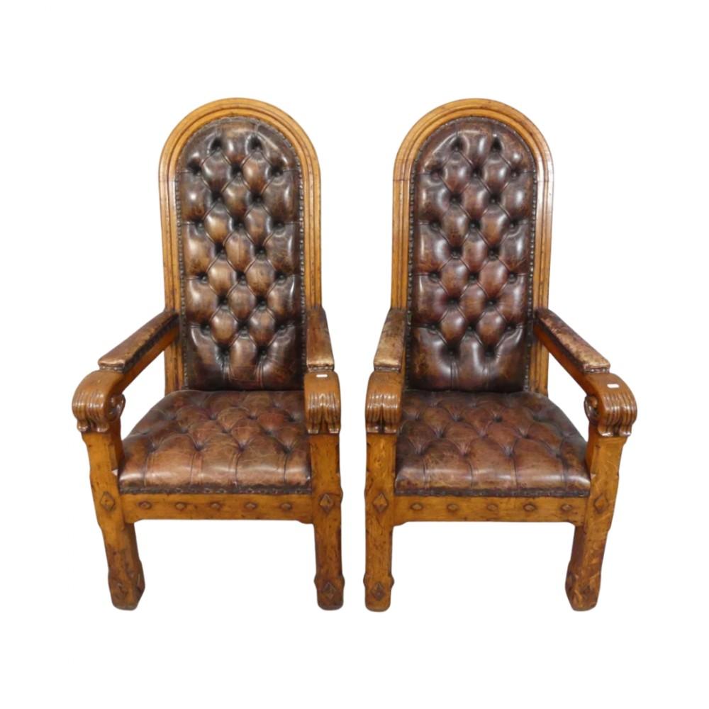 A majestic pair of mid 19th-century Gothic Revival throne-armchairs in solid oak showcasing a lovely original golden patina. Each chair is distinguished by a tall, arched back, upholstered in deep-buttoned soft leather, secured with decorative brass