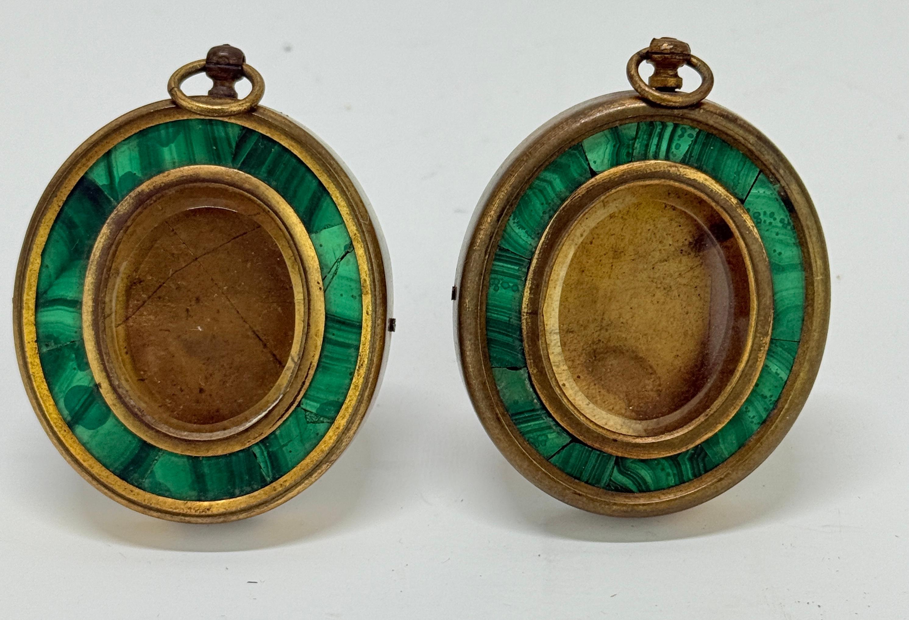 Ognuno di questi medaglioni ovali dell'era Grand Tour è composto da bronzo patinato e incastonato con una fascia di mosaico di malachite intarsiato, che incornicia uno scomparto centrale smaltato per un ritratto in miniatura o un ricordo. La parte