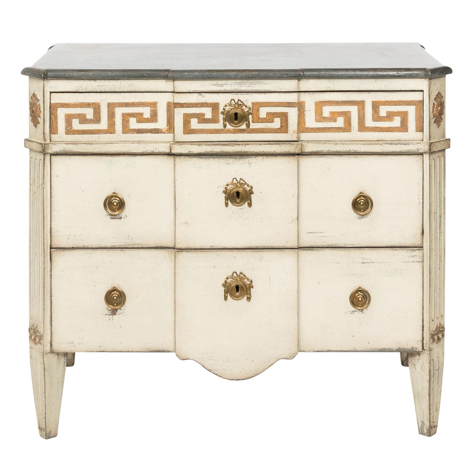Swedish Gustavian style pair of grey painted three drawer commodes with gilded Greek key border, black faux stone top, fluted corners, and brass medallion hardware, circa 19th century. Pieces are signed on the back.
 