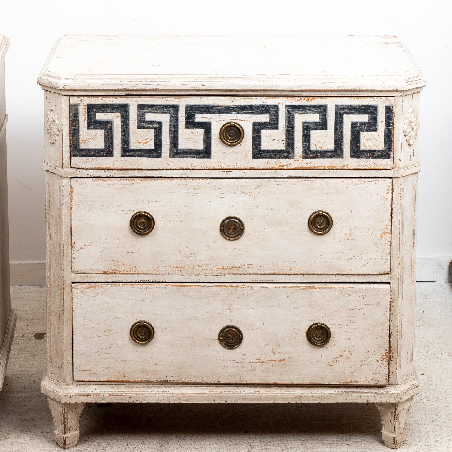 Circa 19th century pair of Swedish Gustavian style commodes with three large horizonal drawers, round metal pulls, and Greek key trim on the top drawer front. The body of commode is further detailed with chamfered corners and rosette motifs. Origin