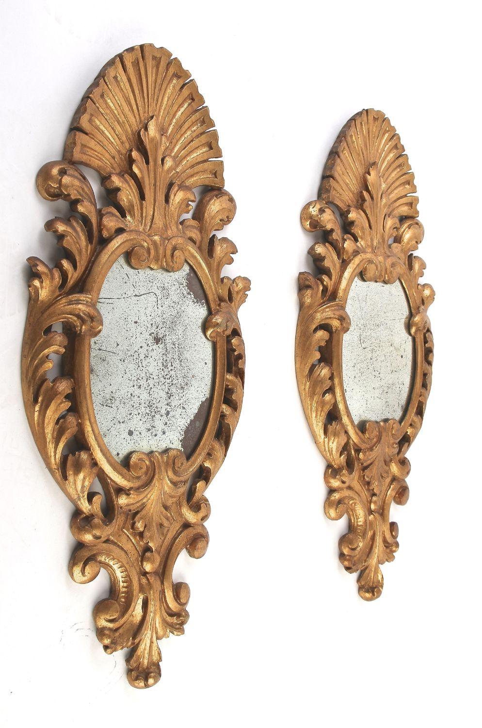 Remarkable pair of amazing crafted gilt wall mirrors from the mid 19th century in Italy. Elaborately hand carved out of basswood around 1850, these outstanding antique gilt mirrors show an absolute enchanting, elongated design with fantastic shaped