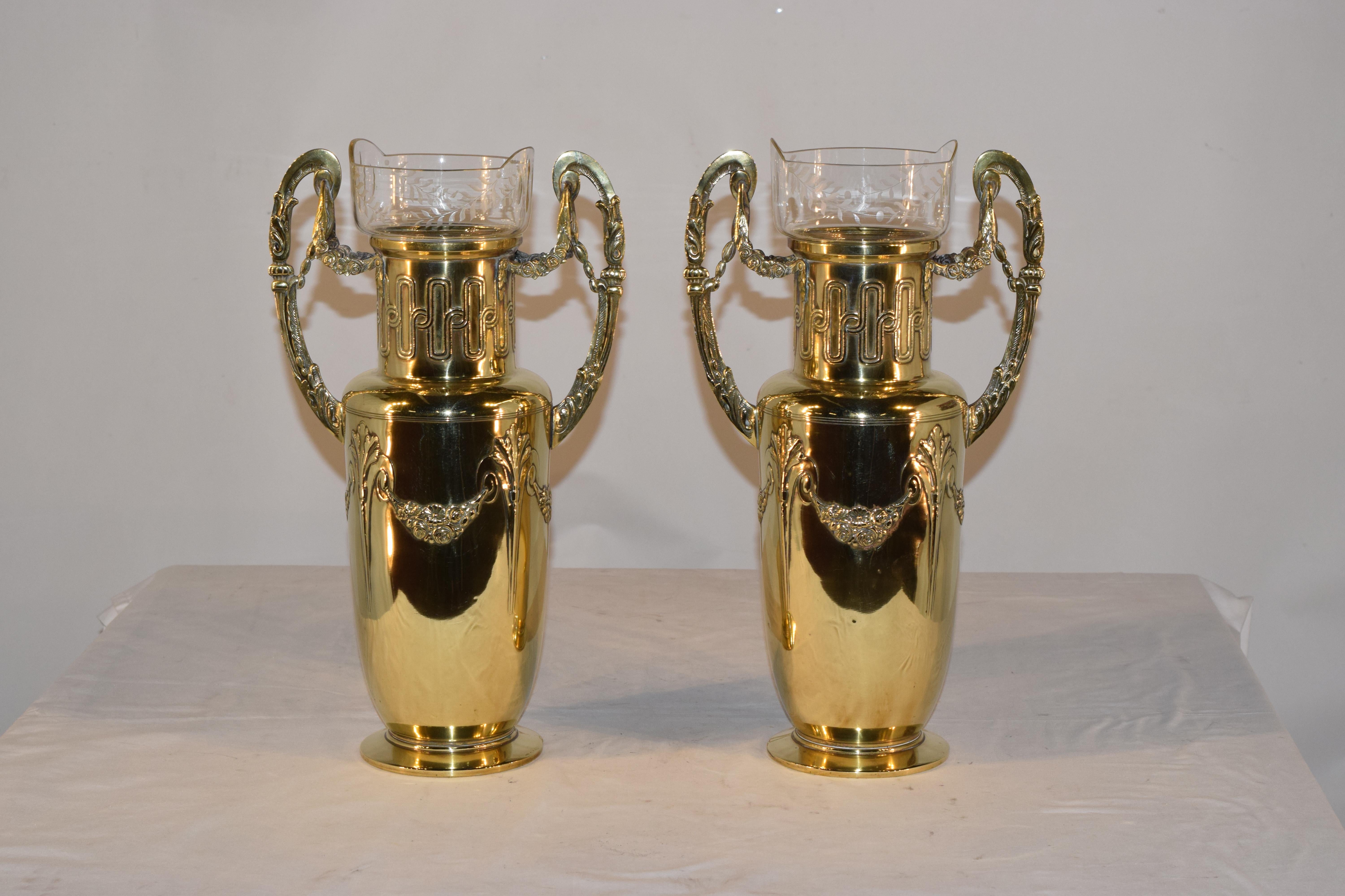 Pair of 19th century hand cast brass vases with elegantly shaped handles which have floral swags and columns, connected to the bases, which are decorated with geometric shapes and acanthus leaf shapes, joined by floral swags. The vases retain their