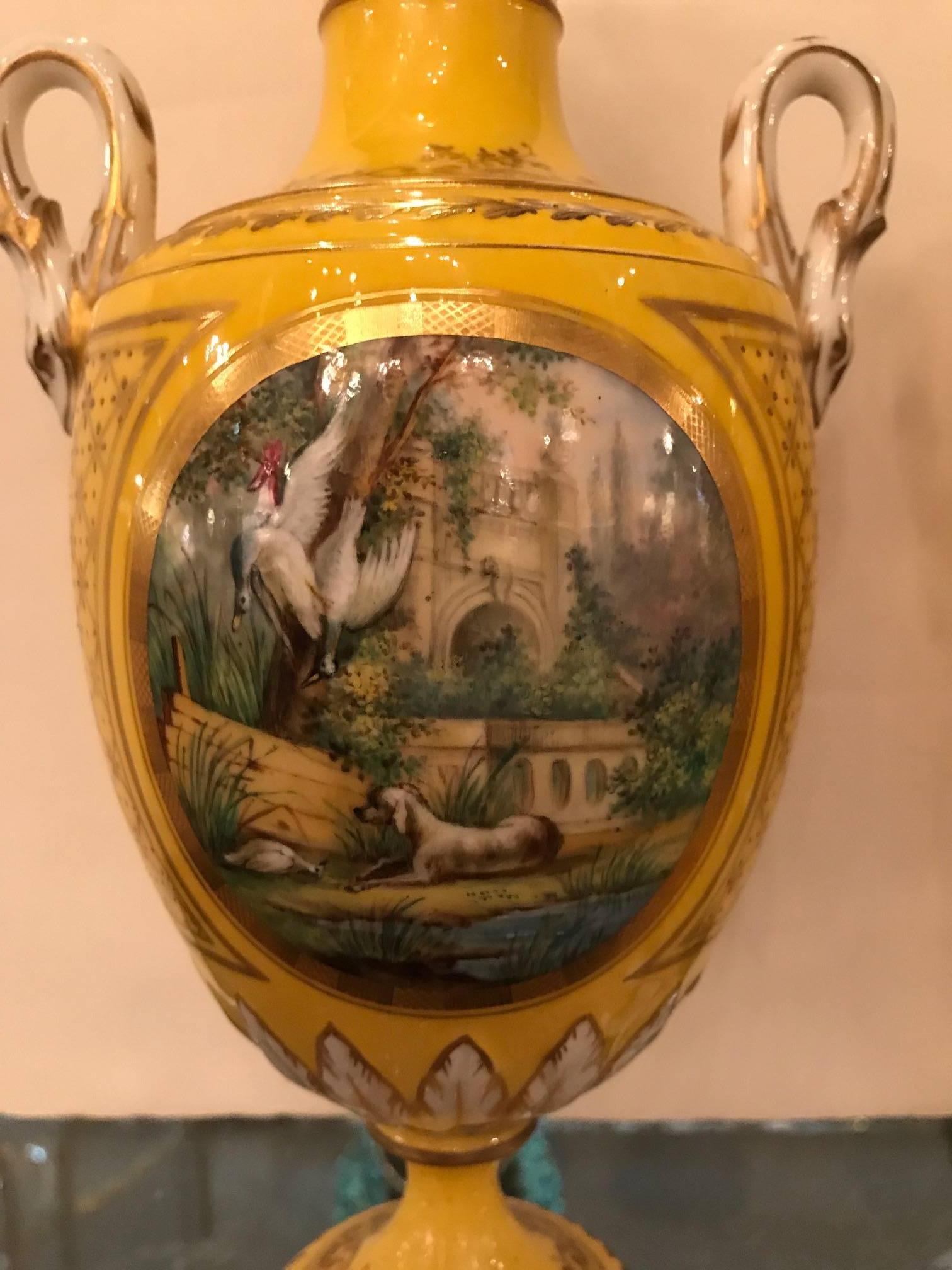 Stunning pair of hand painted and gilt porcelain urns. The vibrant yellow background with detailed cartouches on the fronts and backs depicting French County life. The sides are in a gilt lattice pattern with gilt decoration all-over. These urns