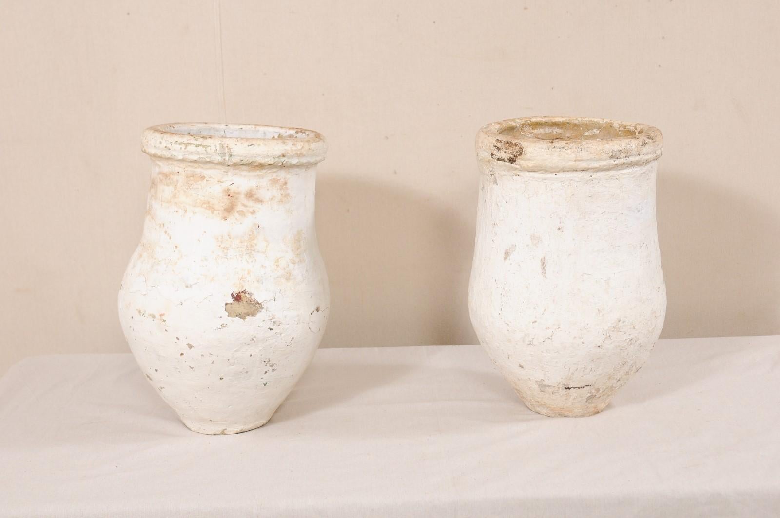 A Spanish pair of clay jars from the 19th century. This pair of antique jars from Spain have gracefully handmade bulbous bodies, with rounded lips, and rest upon flat, rounded bases. They are primarily white and cream, with some chipping and a