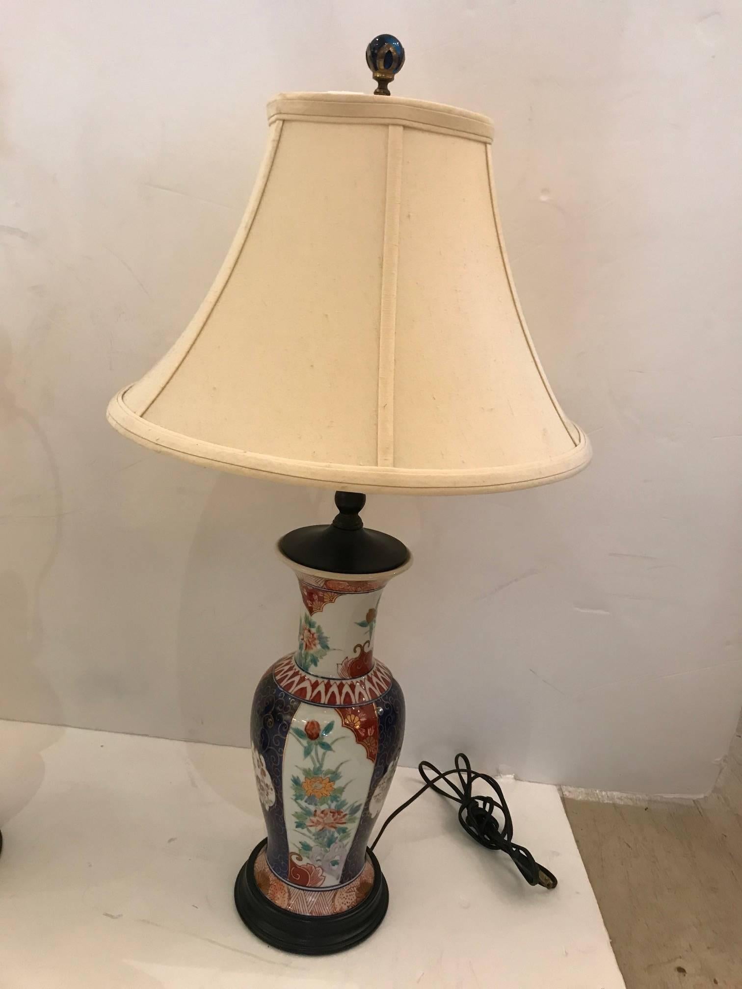 Very elegant pair of antique Imari table lamps having vase shaped bases adorned with beautiful patterns of flowers in green cream and cinnarbar, with gold curlicues against a striking saffire blue. The bases are wood, 7 inches round, and the finials