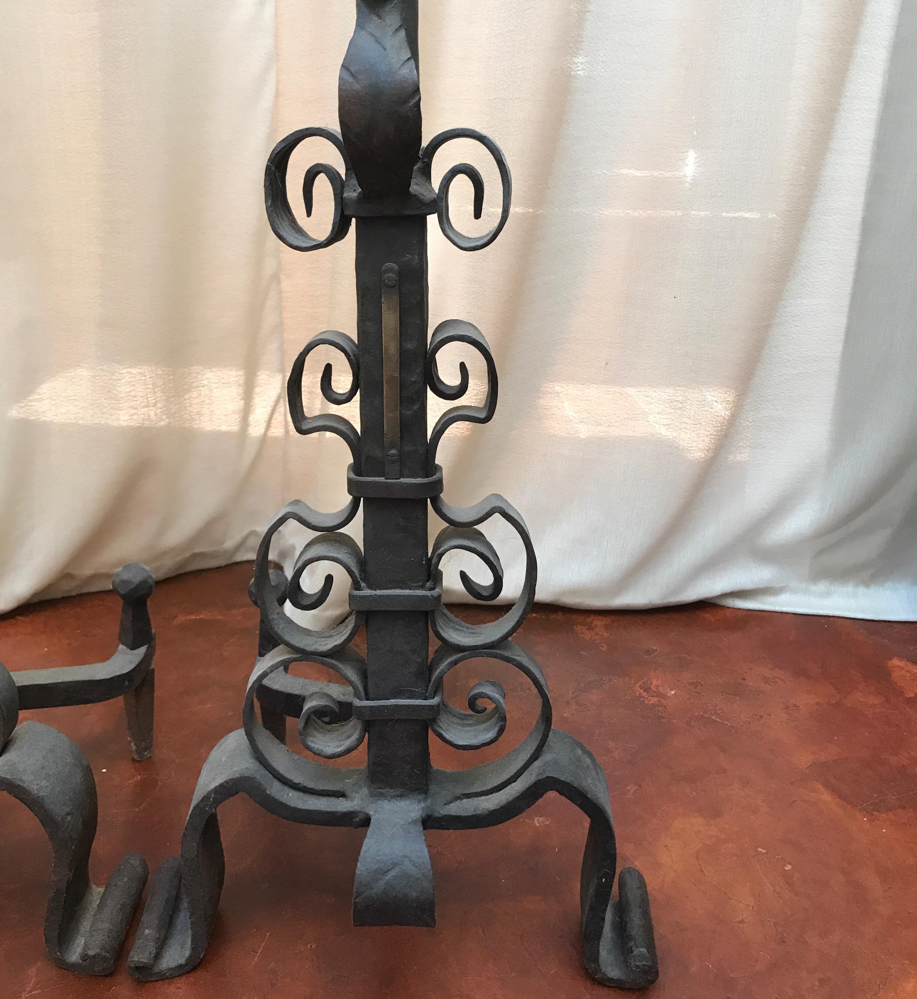 This pair of andirons are very heavy and large made of Iron and brass from the 19th century. The scroll work continuous down the center shaft and they rest on two feet with a curved iron leg. On the top of the andirons are brass balls held with a