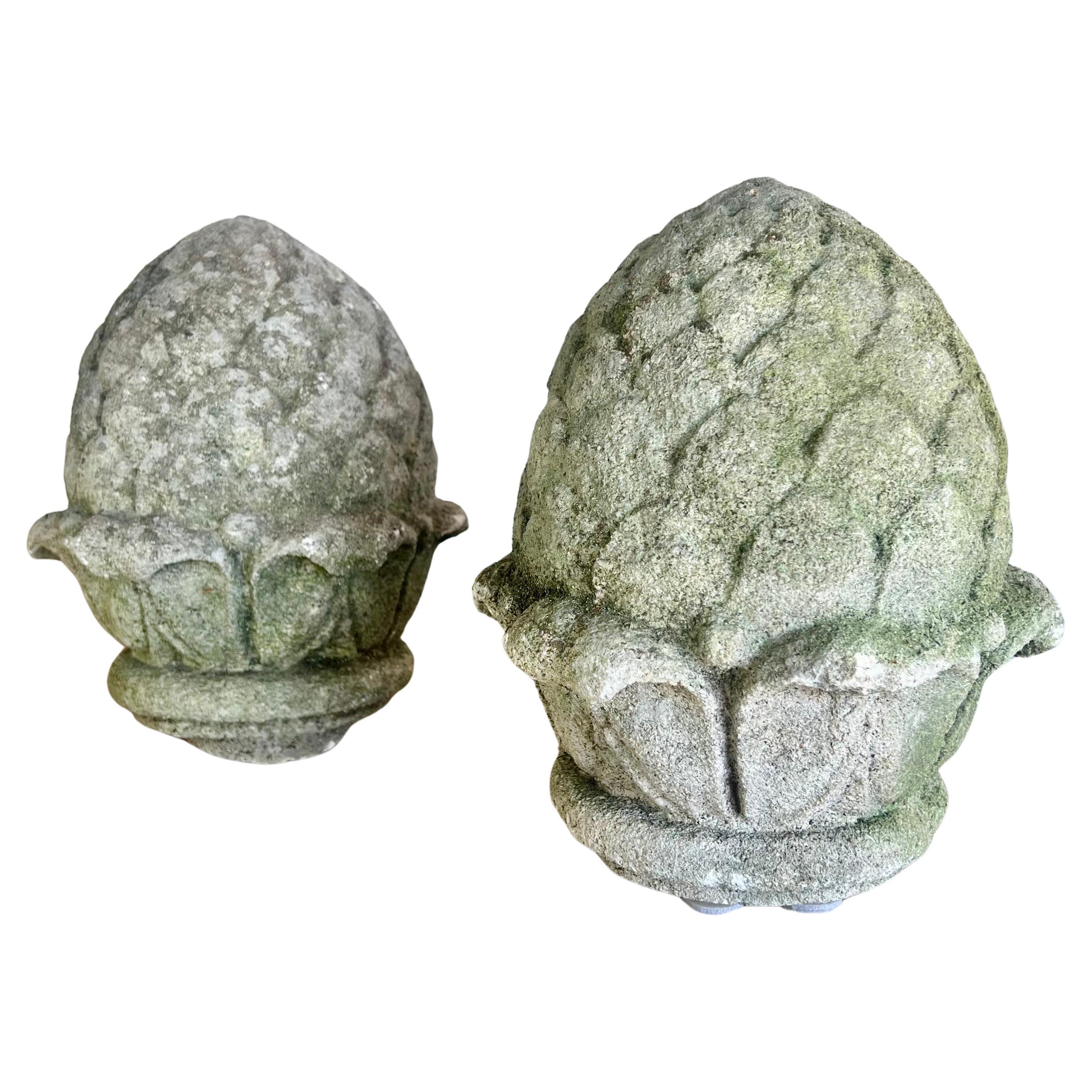 A pair of neoclassical Italian-style cement artichokes with a moss patina.  The moss patina adds a touch of antiquity and natural grace, suggesting age and blending seamlessly with garden environments or adding a rustic touch to more modern