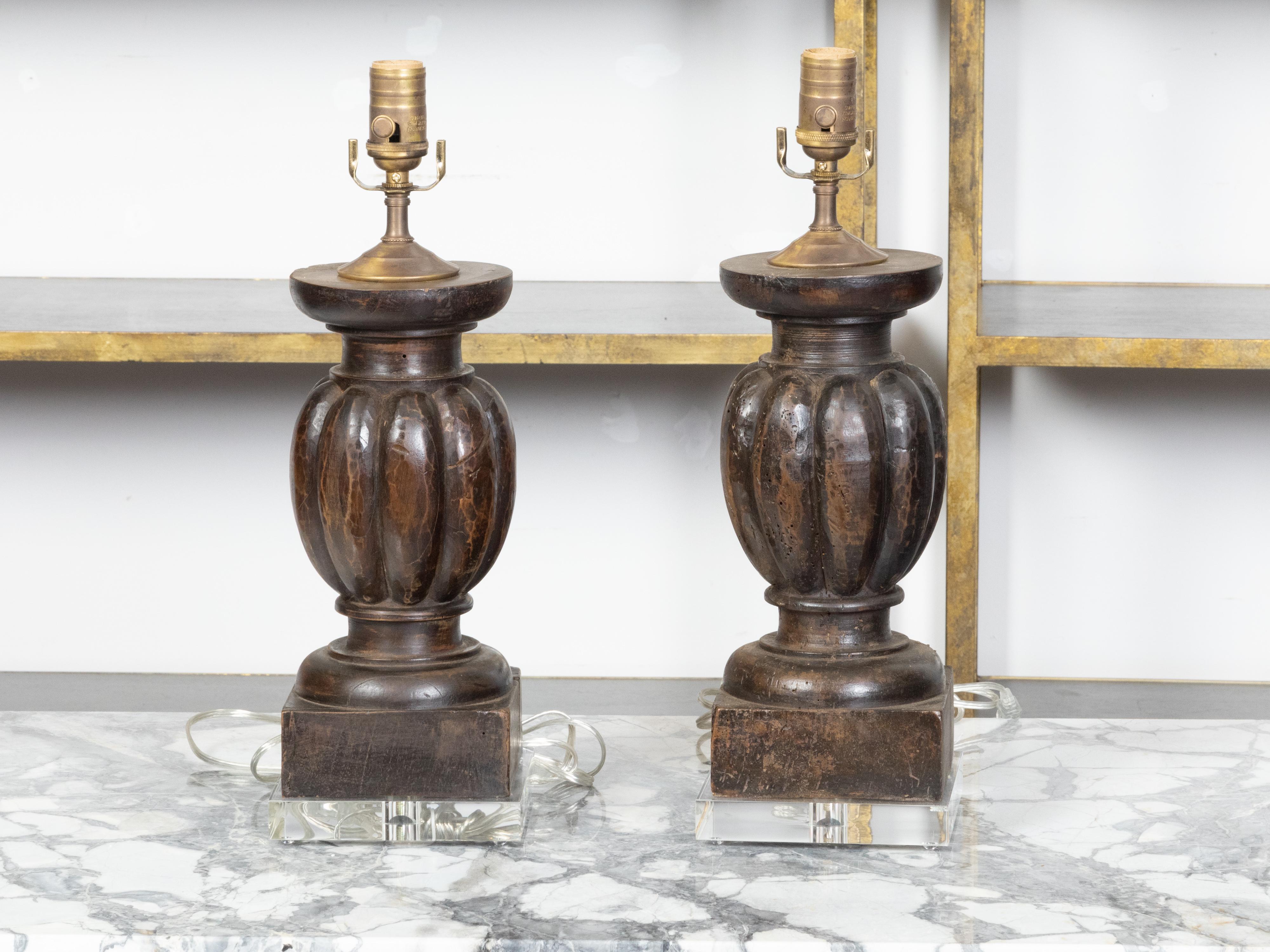 A pair of Italian carved walnut fragments from the 19th century depicting balusters with gadroon motifs, made into US wired table lamps mounted on square lucite bases. Created in Italy during the early years of the 19th century, each of this pair of