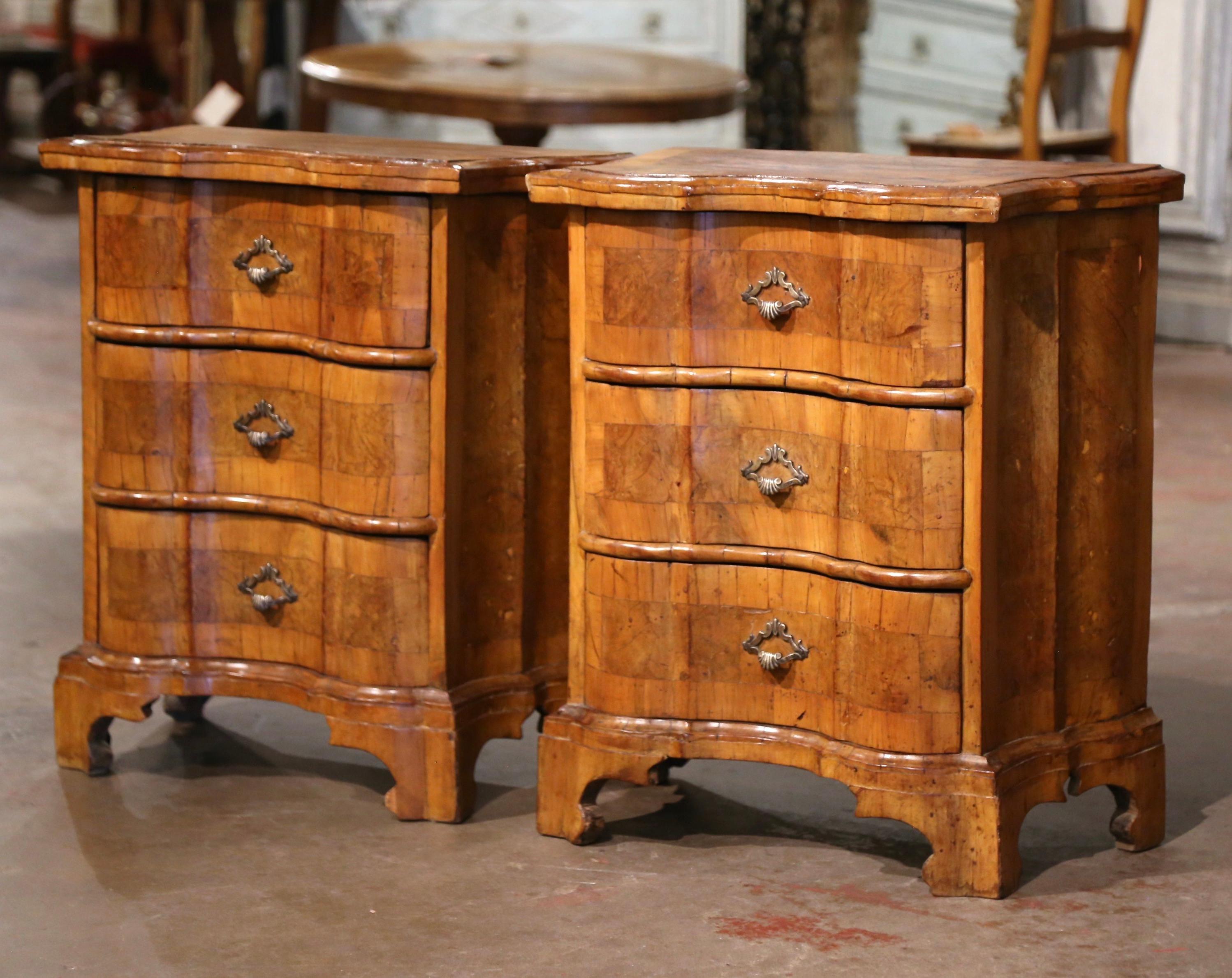 Decorate a master bedroom with this elegant pair of antique nightstands. Crafted in Italy circa 1820, each chest stands on scrolled bracket feet over a canted form case. The cabinet features three serpentine drawers decorated with inlaid marquetry