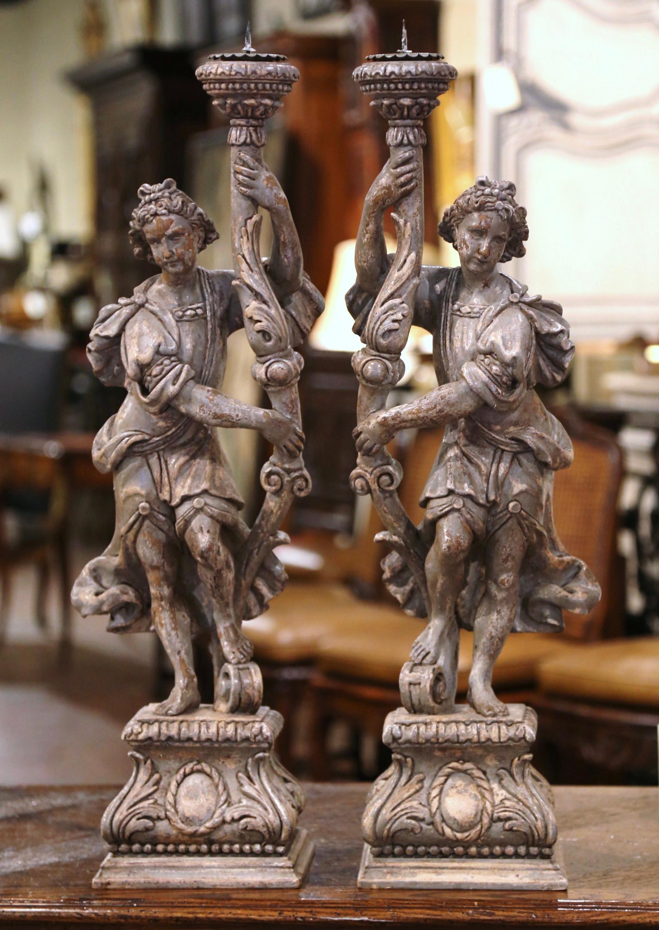 Decorate a console, buffet or mantel with this pair of elegant antique candle holders. Crafted in Italy circa 1880, and built of solid oak, the candlesticks stand on a square base decorated with acanthus leaf motifs. Each neoclassical figure depicts