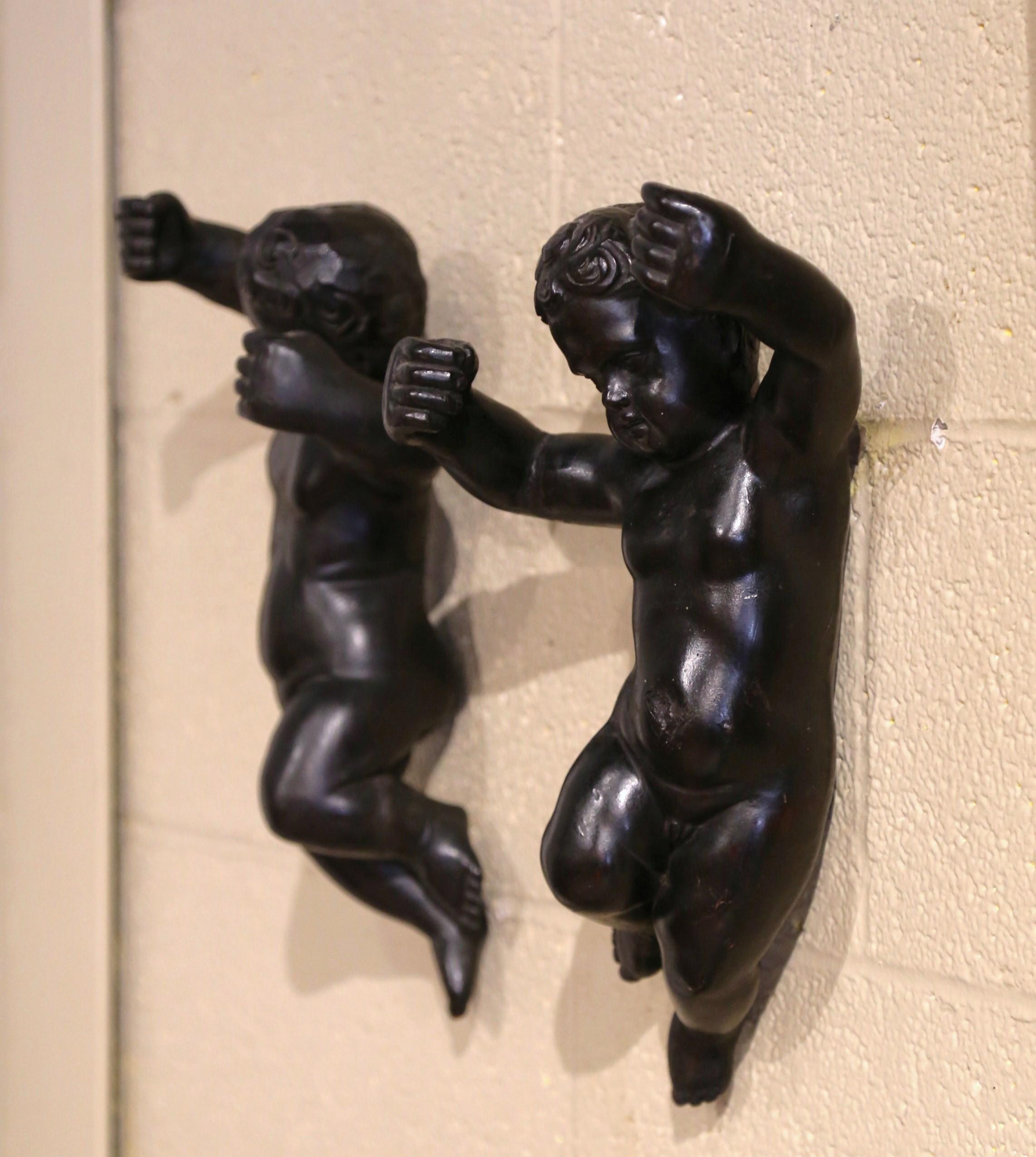 These elegant antique putti sculptures were crafted in Italy circa 1860; each cherub wall hanging sculpture feature a hand carved cherub in the nude with short curly hair. Hand painted in black, the cherub's arms are raised in exultation. It appears