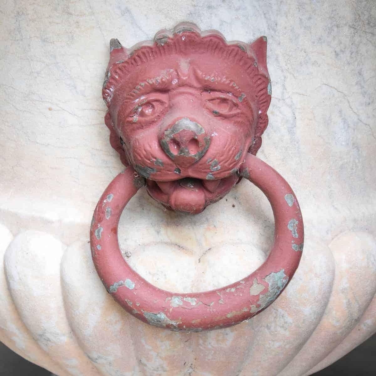 Coppia di urne in marmo scolpito con il tema iconico dei leoni che stringono in bocca degli anelli. Le urne sono in marmo italiano di Carrara del XIX secolo, in stile piedistallo.  I leoni in bronzo sono stati dipinti di rosso terracotta. Venduto in