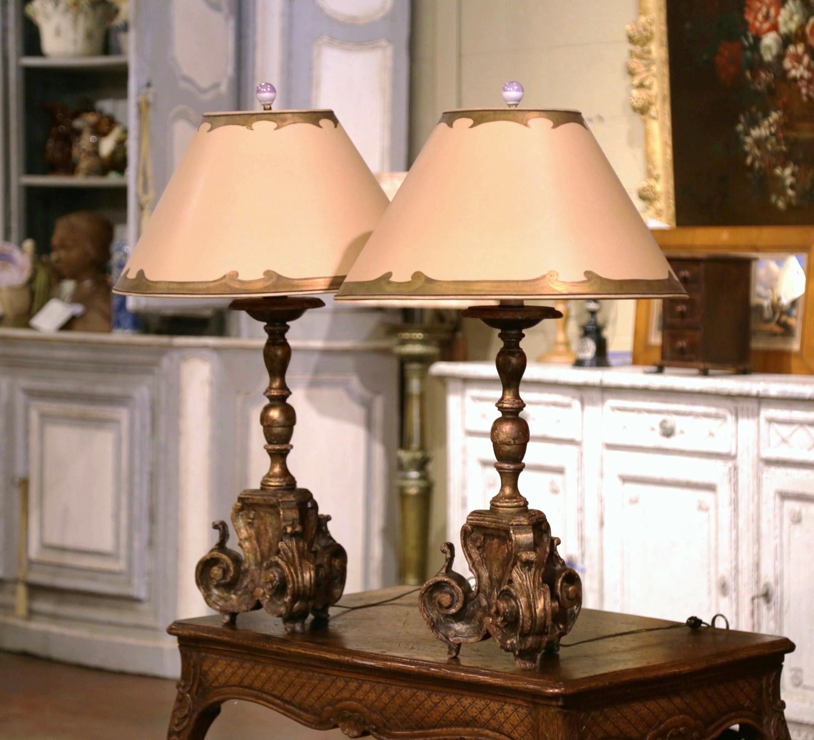 Add an air of drama and elegance to your home with this pair of antique table lamps. Crafted in Italy circa 1870 and converted into table lamps, each candlestick stands on a tripod base decorated with a carved medallion, and ending with scrolled