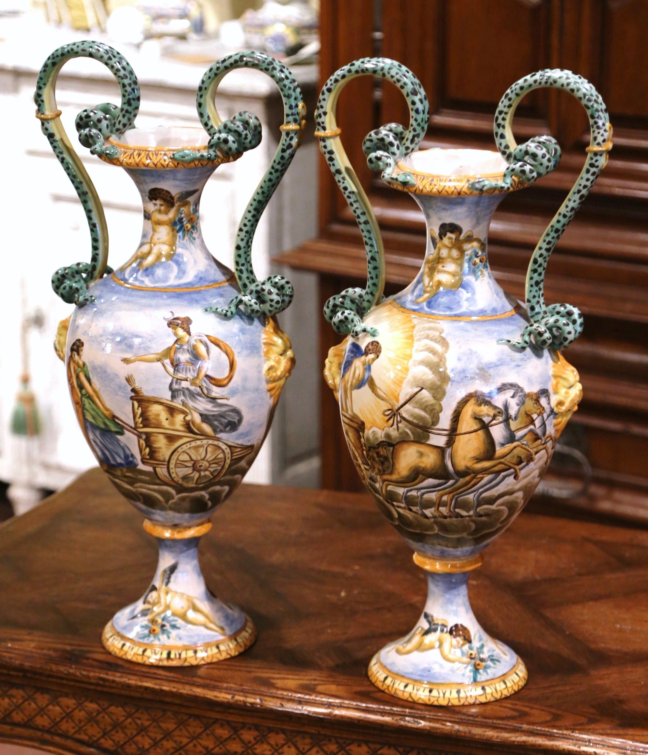 This delicate pair of antique porcelain vases were sculpted in Italy, circa 1870. Each classical vase stands on round base decorated with hand painted cherubs; each vessel is supported with scrolled snake form handles over a long neck, also