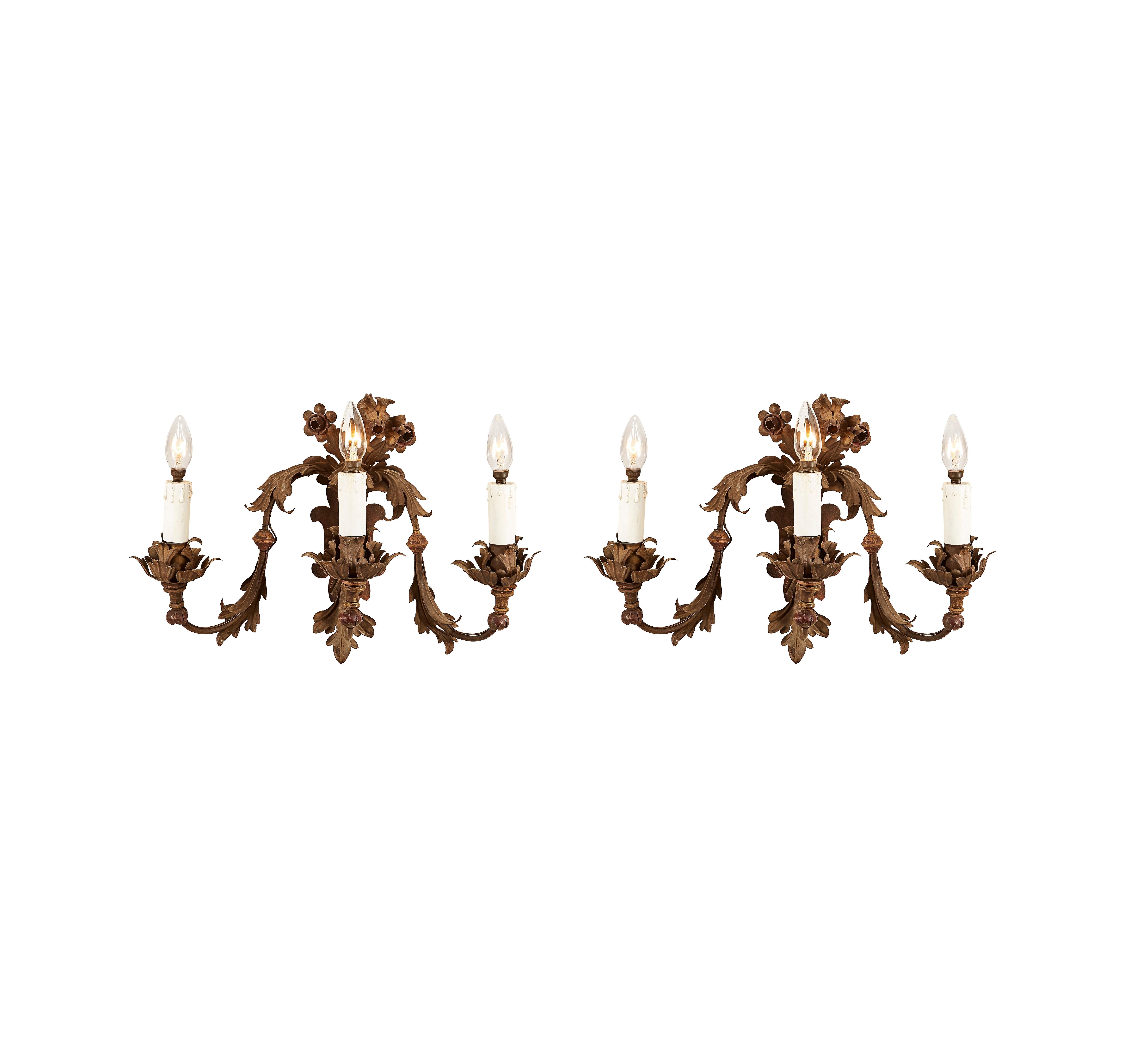 Pair of antique three-light wrought iron wall lights dating back to the late-19th century. This Italian artwork is fully handmade, featuring three wrought iron curved arms, decorated throughout with leaves and topped in the upper part by flowers.