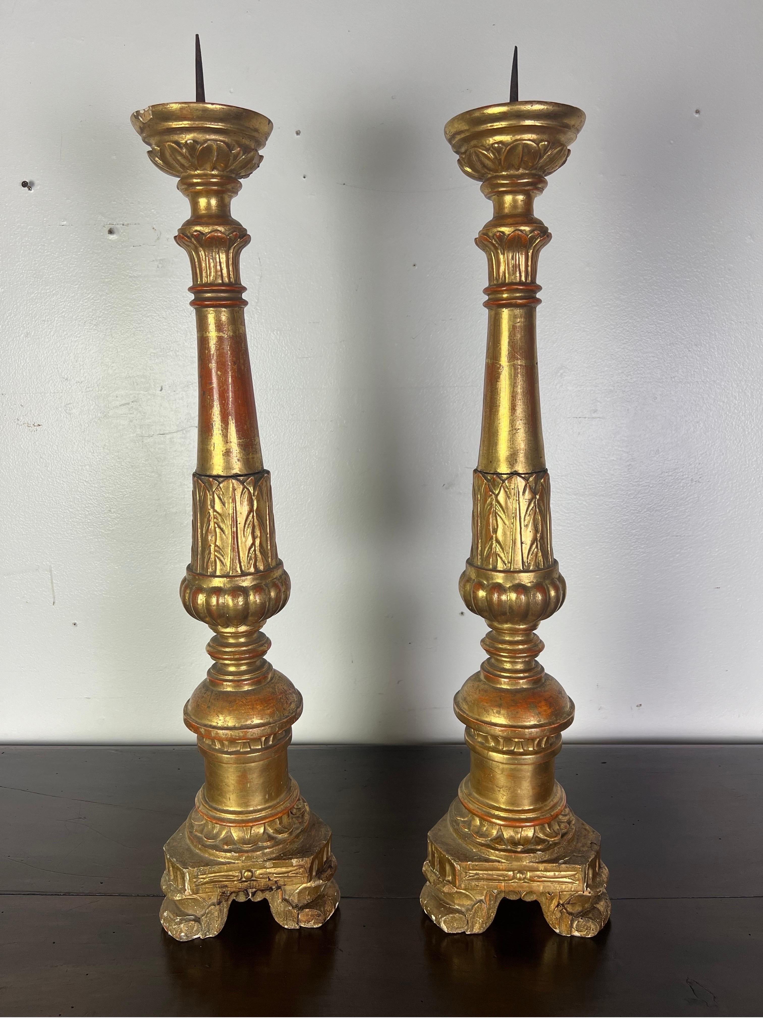 A 19th-century pair of Italian giltwood candlesticks with prickets and a beautifully carved acanthus leaf design throughout is a testament to the opulent and detailed craftsmanship of the period.  Giltwood refers to wood that has been gilded-covered