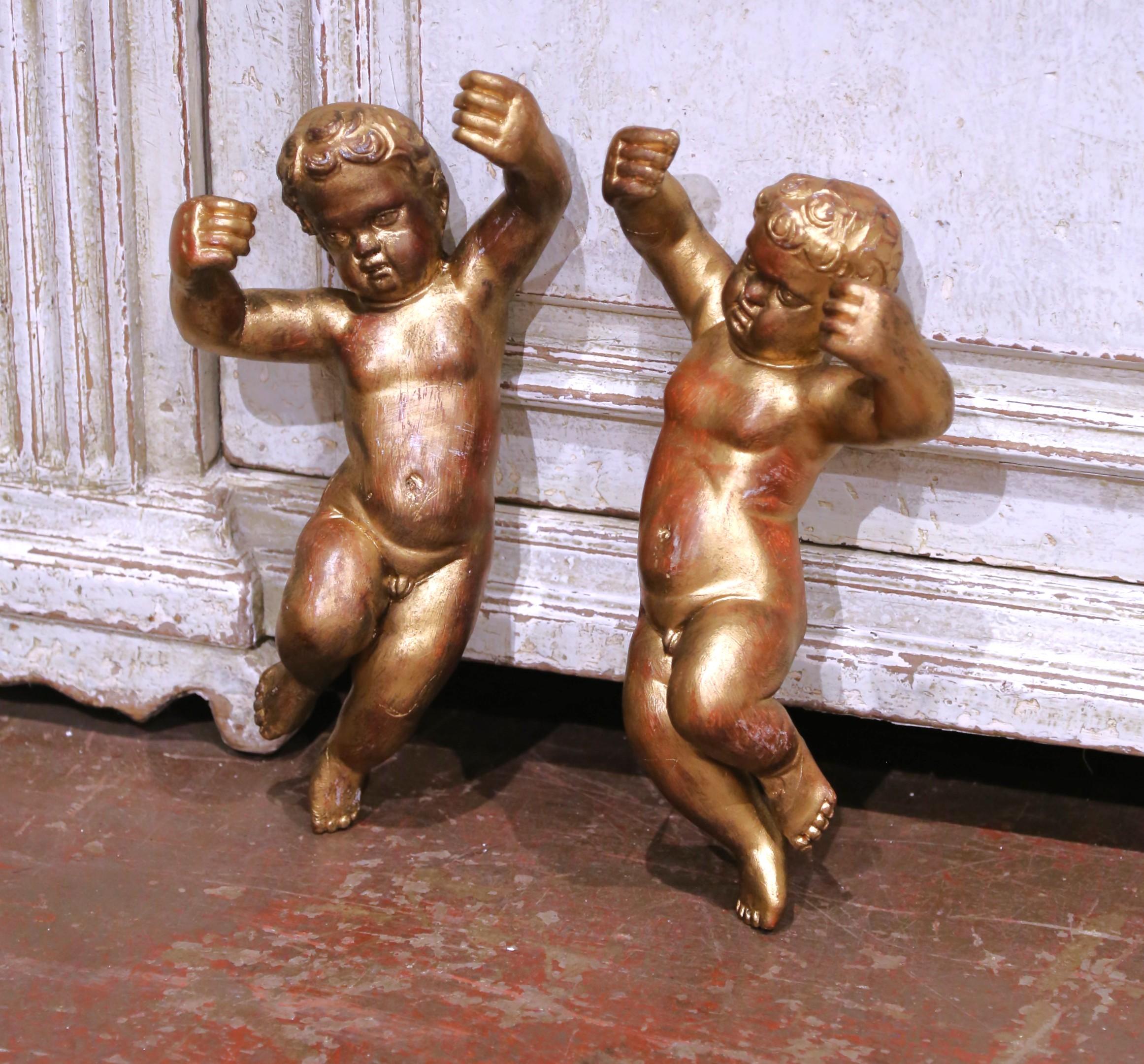 Décorez un salon, une entrée ou un coin de chapelle avec cette paire expressive d'angelots italiens anciens suspendus au mur, sculptés en Italie vers 1860 et finis en bois doré richement bruni. Chaque putti est représenté dans un mouvement gracieux,