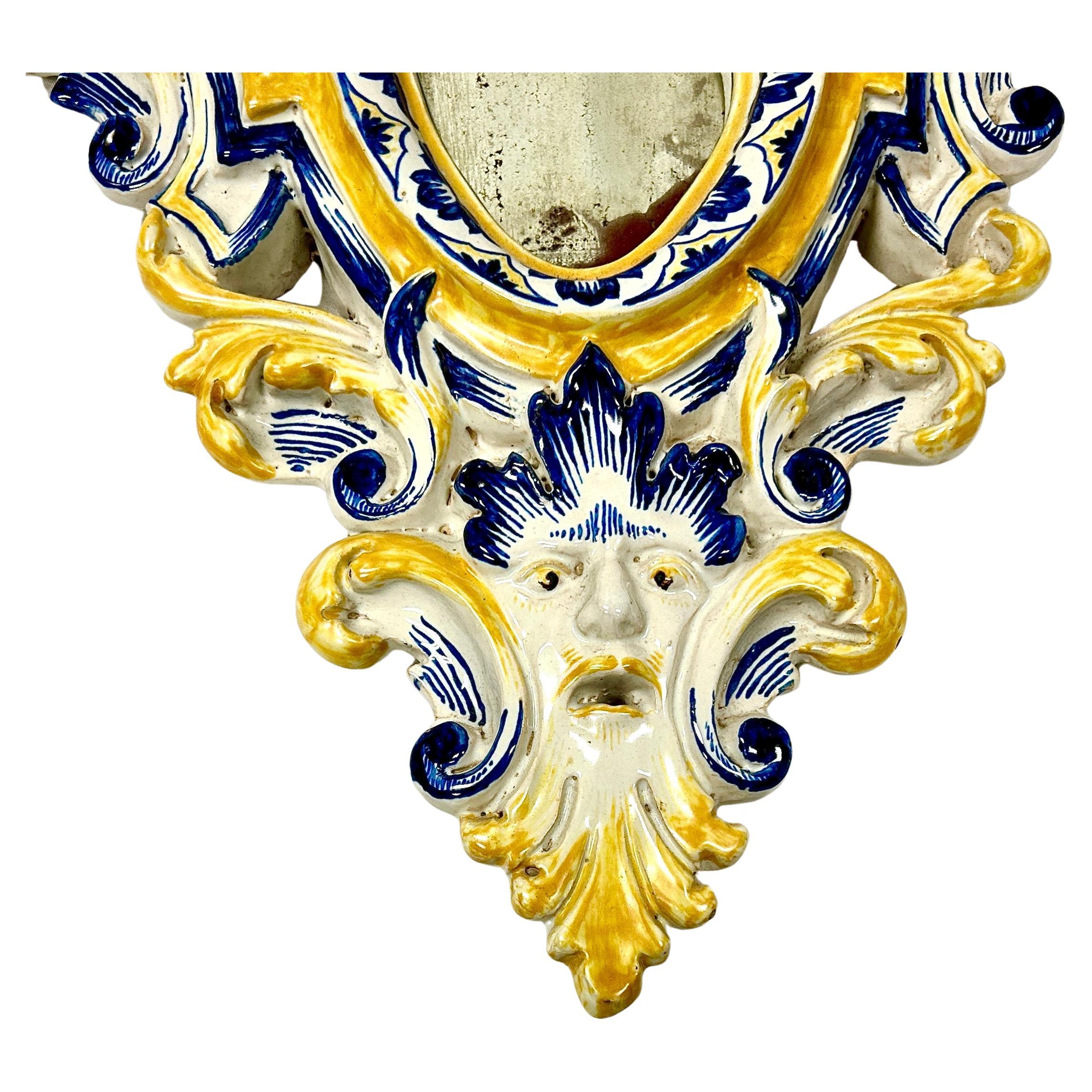 Feines Paar italienischer Majolika-Spiegel aus dem 19. Jahrhundert mit Glasur. Die Spiegel sind handgefertigt und in den Farben Weiß, Gelb und Blau gehalten, mit geschnitzten Rändern, jeweils mit einer bärtigen Maske versehen und mit Blumenspritzern