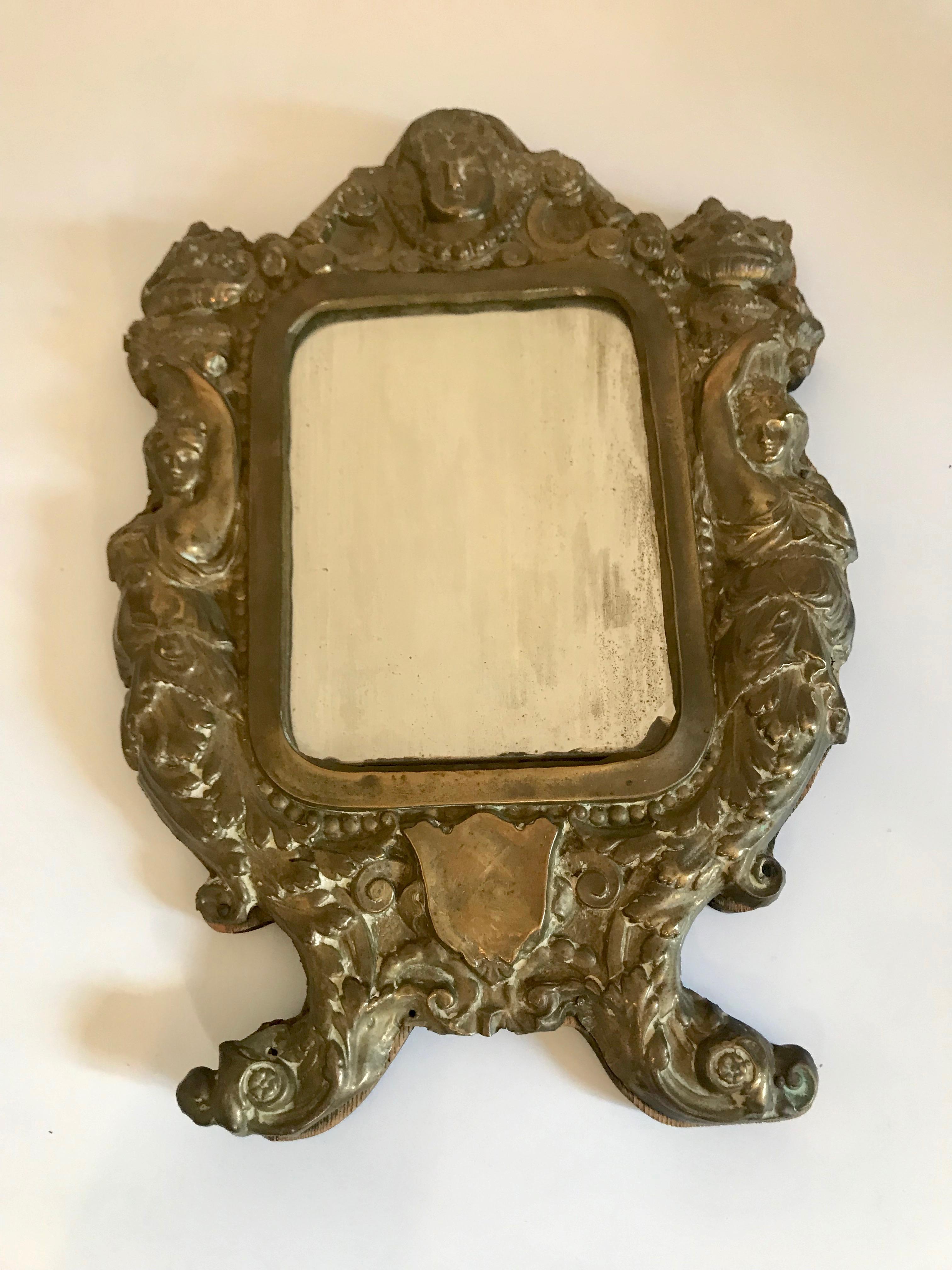 Pair of 19th century Italian mirrors in ornate brass frames. Fits mirror size 4.75 in by 6.25 in. The brass frame design shows a woman and a column on either side, a woman's face on the top, and a shield on the bottom.