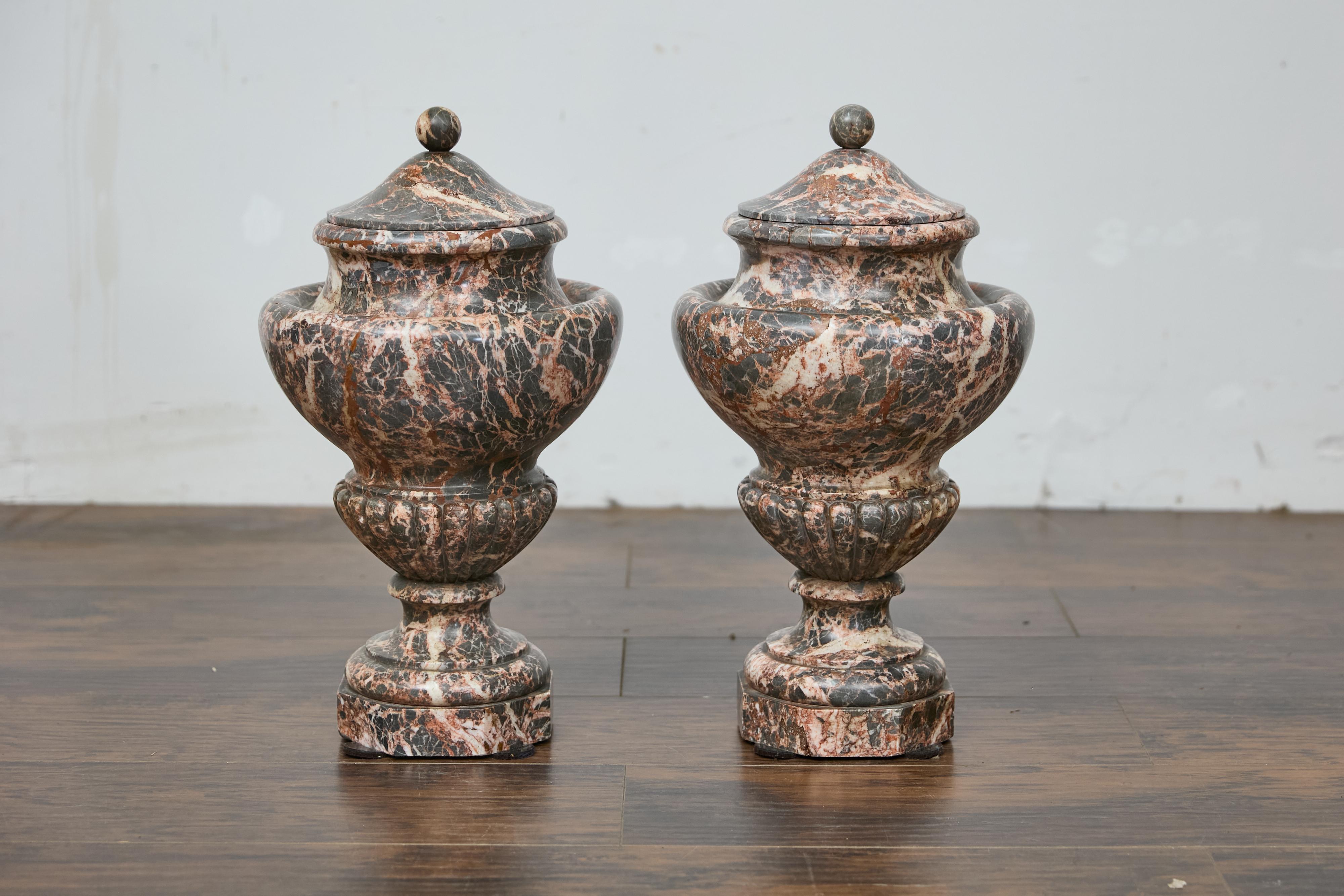 Coppia di urne neoclassiche italiane con coperchio in marmo rosso del XIX secolo. Impregnata di eleganza classica, questa coppia di urne in marmo rosso italiano del XIX secolo cattura la grandezza di un'epoca passata. Scolpita in un marmo riccamente