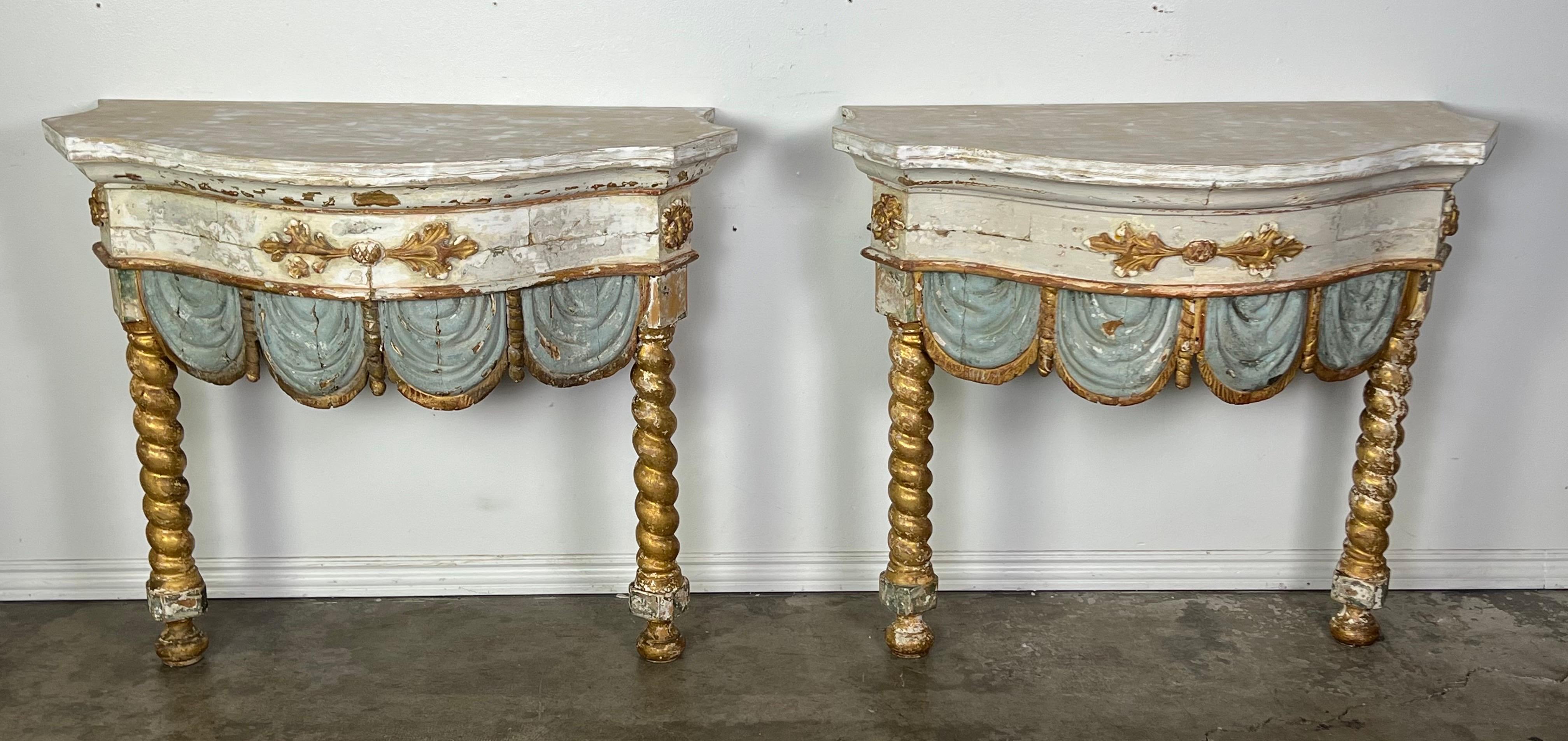 Pair of early 19th century Italian painted and parcel gilt consoles, showcasing the described features such as twisted gilt wood straight legs, blue & gold leaf scalloped apron, and a wood painted top.
